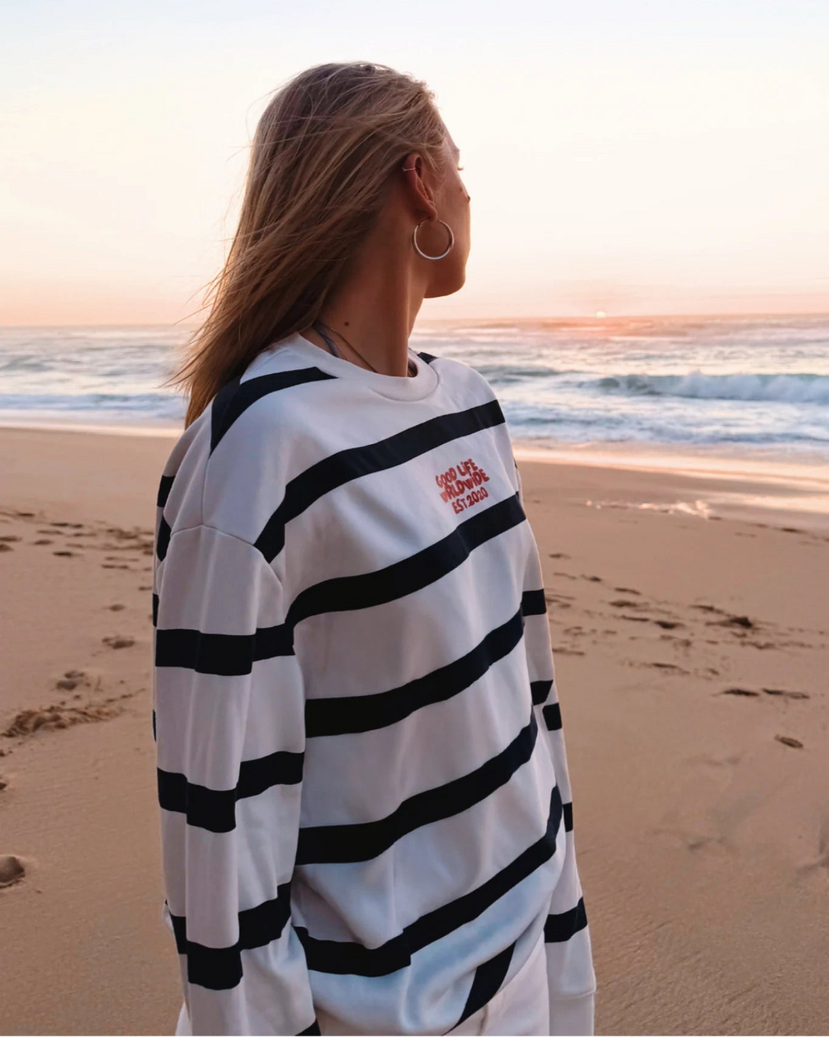 Frau trägt Dockside Rebel Sweater Vintage Cream am Strand bei Sonnenuntergang