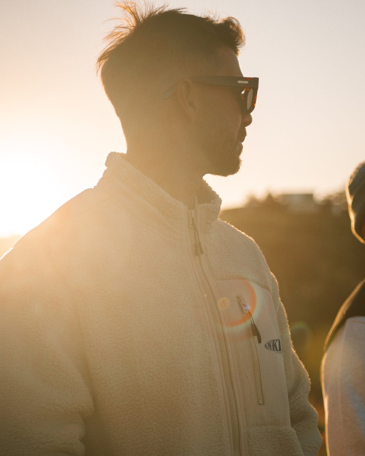 Mann steht vor Sonnenuntergang und trägt fleece jacke in beige
