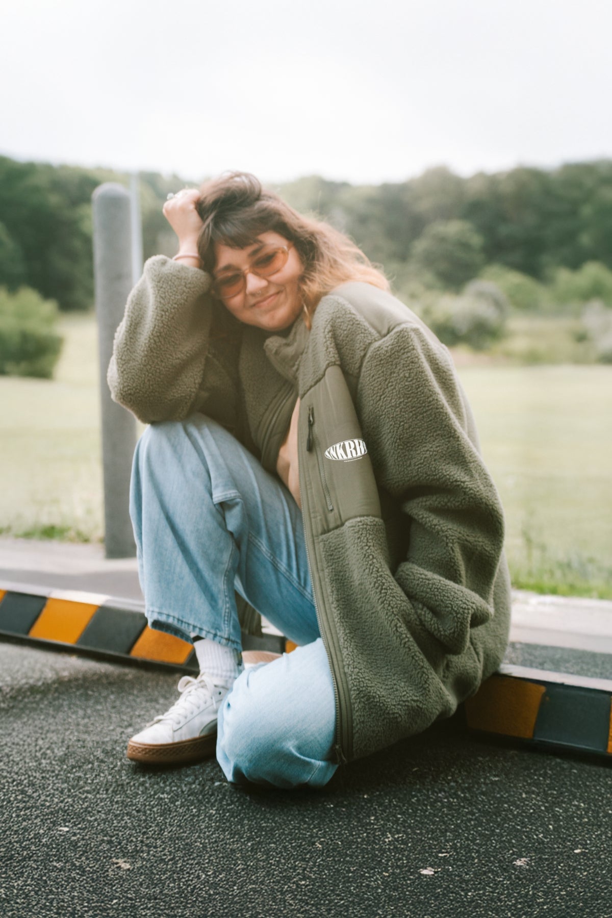 frau sitzt auf boden und lacht in kamera trägt grüne outdoor fleece jacke