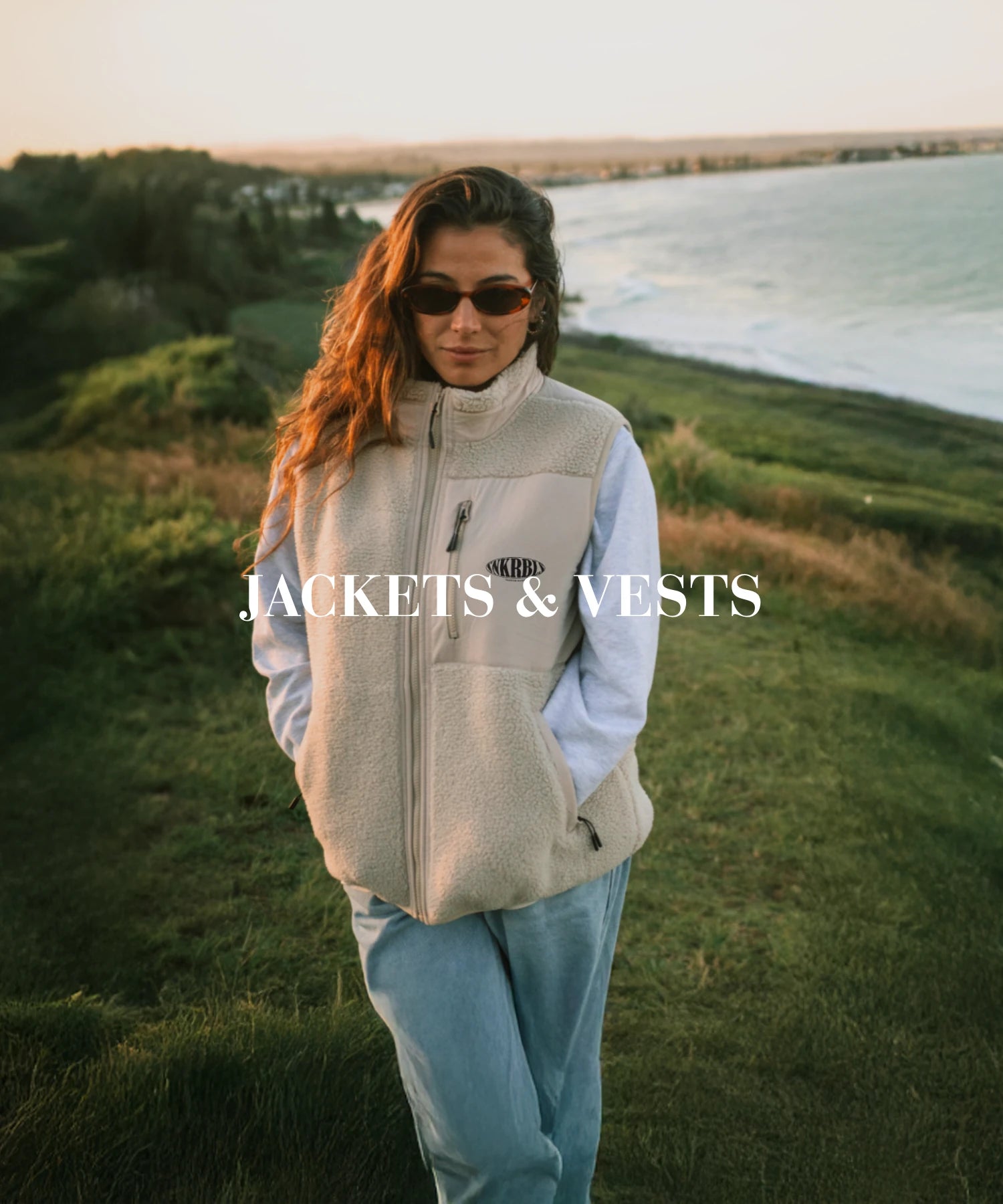 Frau mit Sonnenbrille trägt kuschelige Fleeceweste auf einer Küstenklippe – windfester Outdoor-Style.