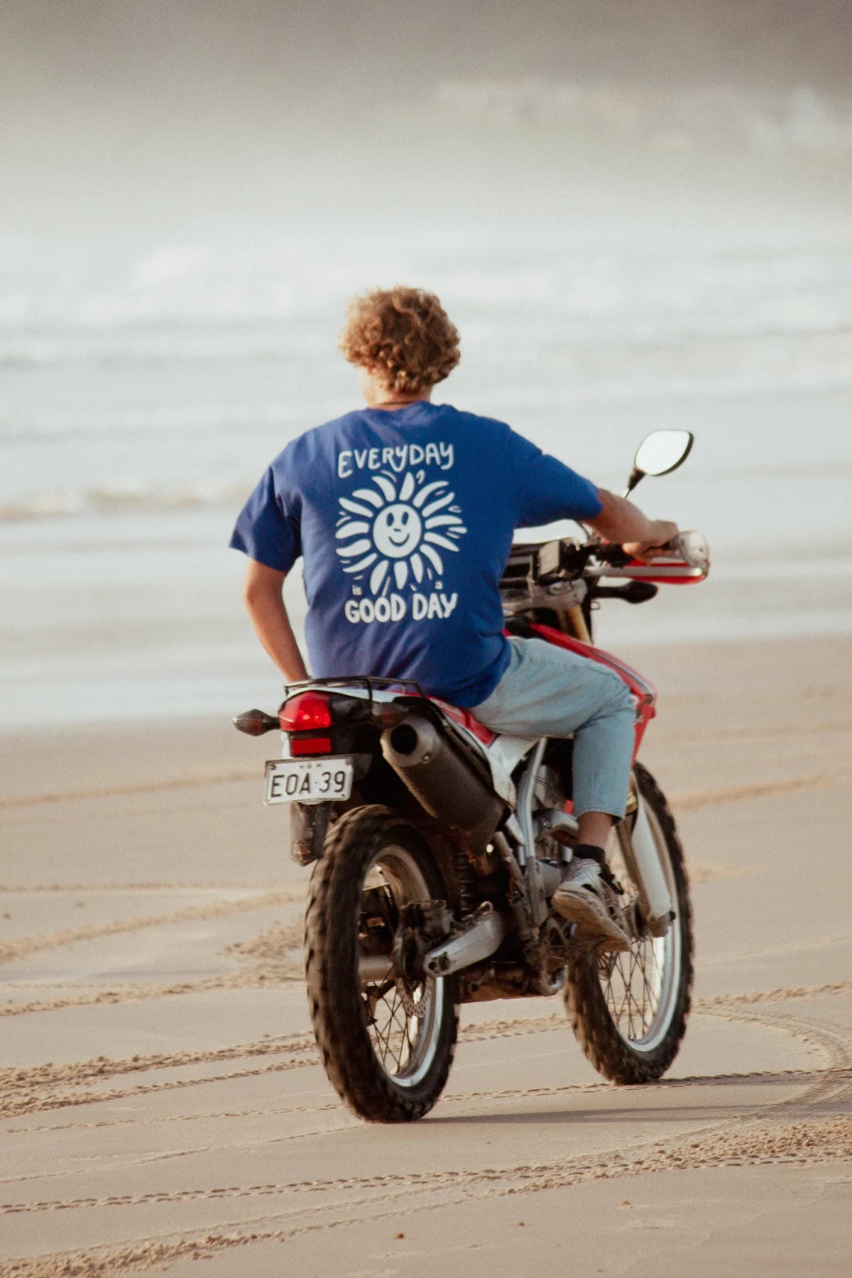 Blaues Oversized T-Shirt mit Everyday Good Day Print auf Motorrad am Strand