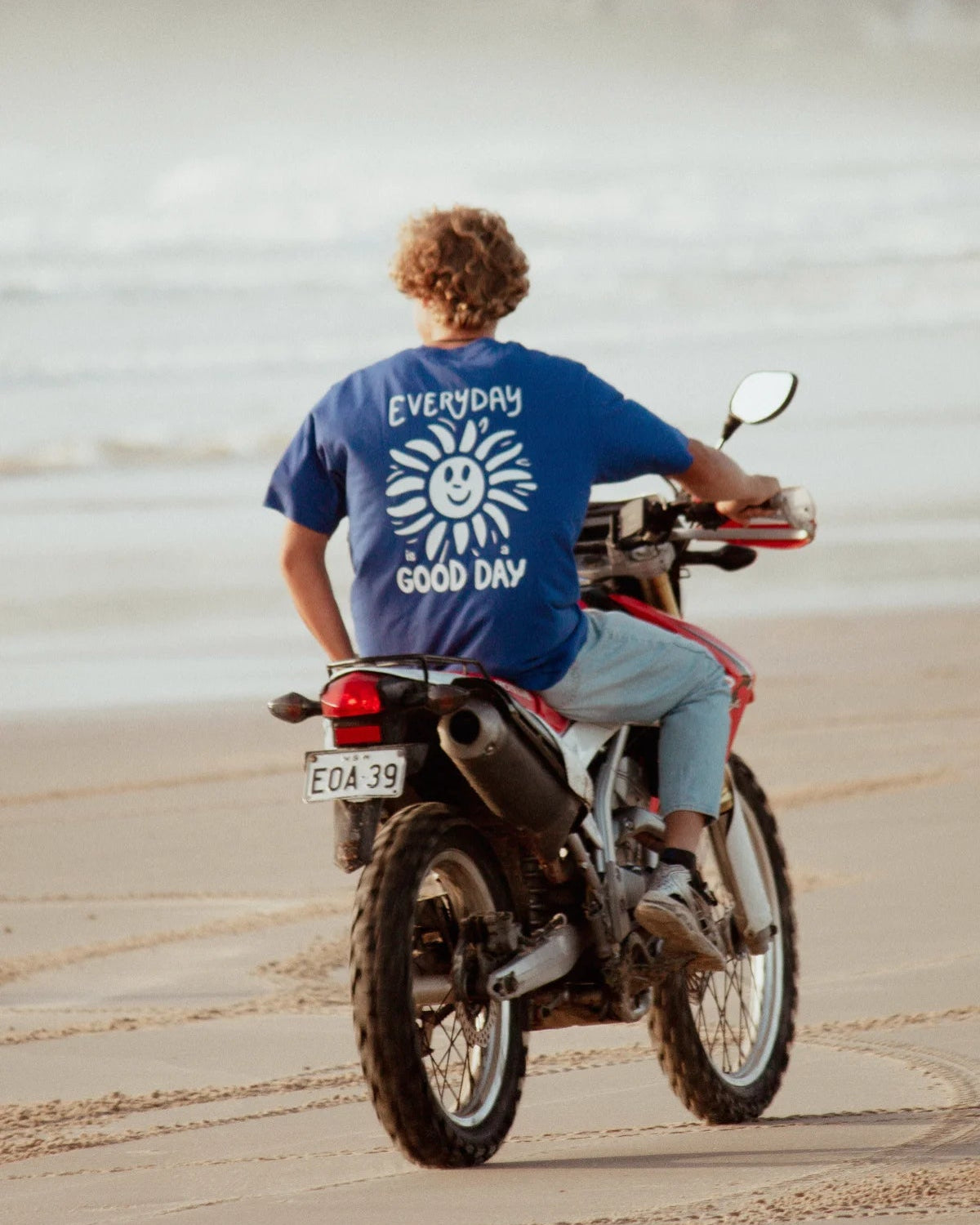 Blaues Oversized T-Shirt mit Everyday Good Day Print auf Motorrad am Strand