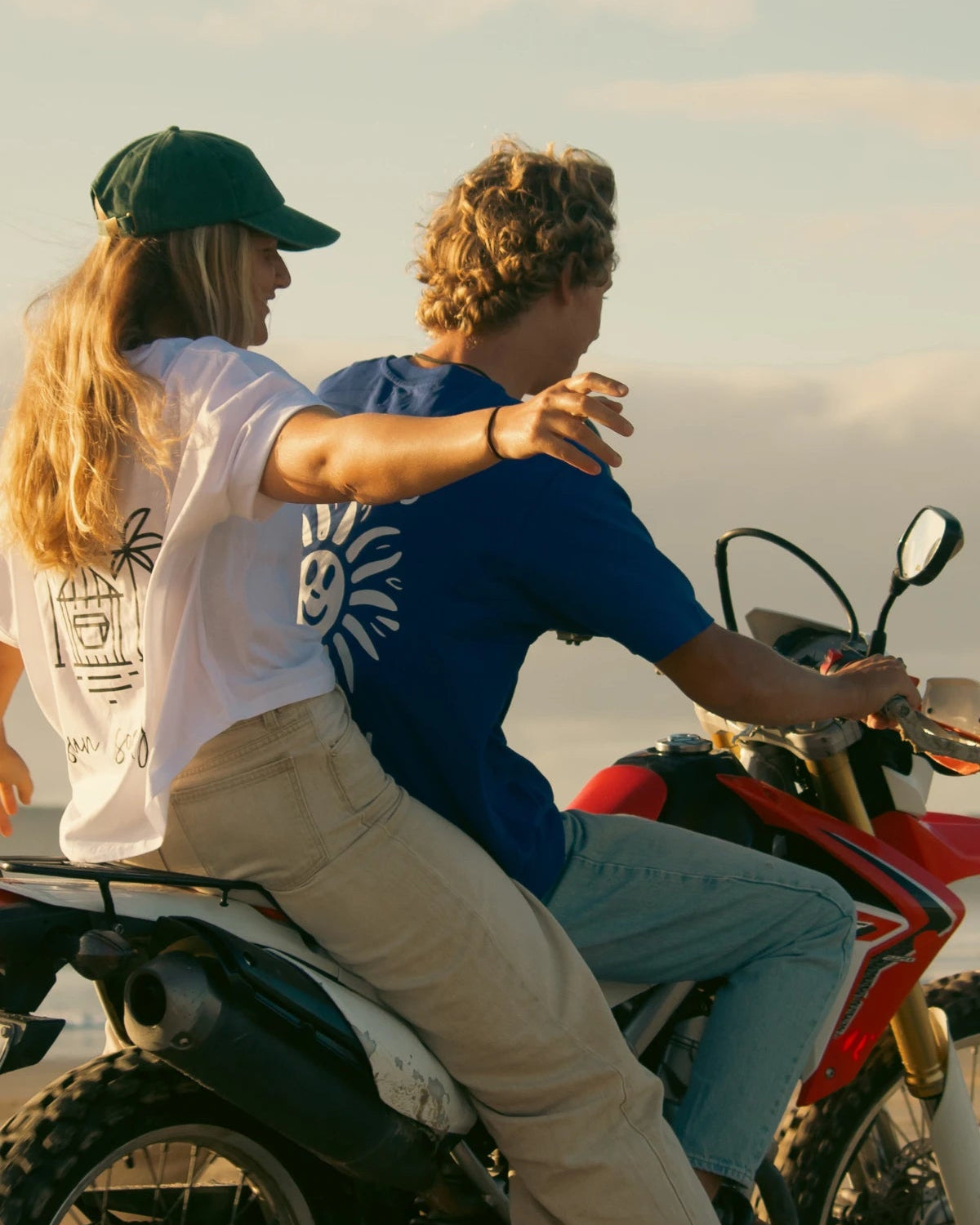 Paar auf Motorrad mit blauem Good Day T-Shirt vor Küstenkulisse
