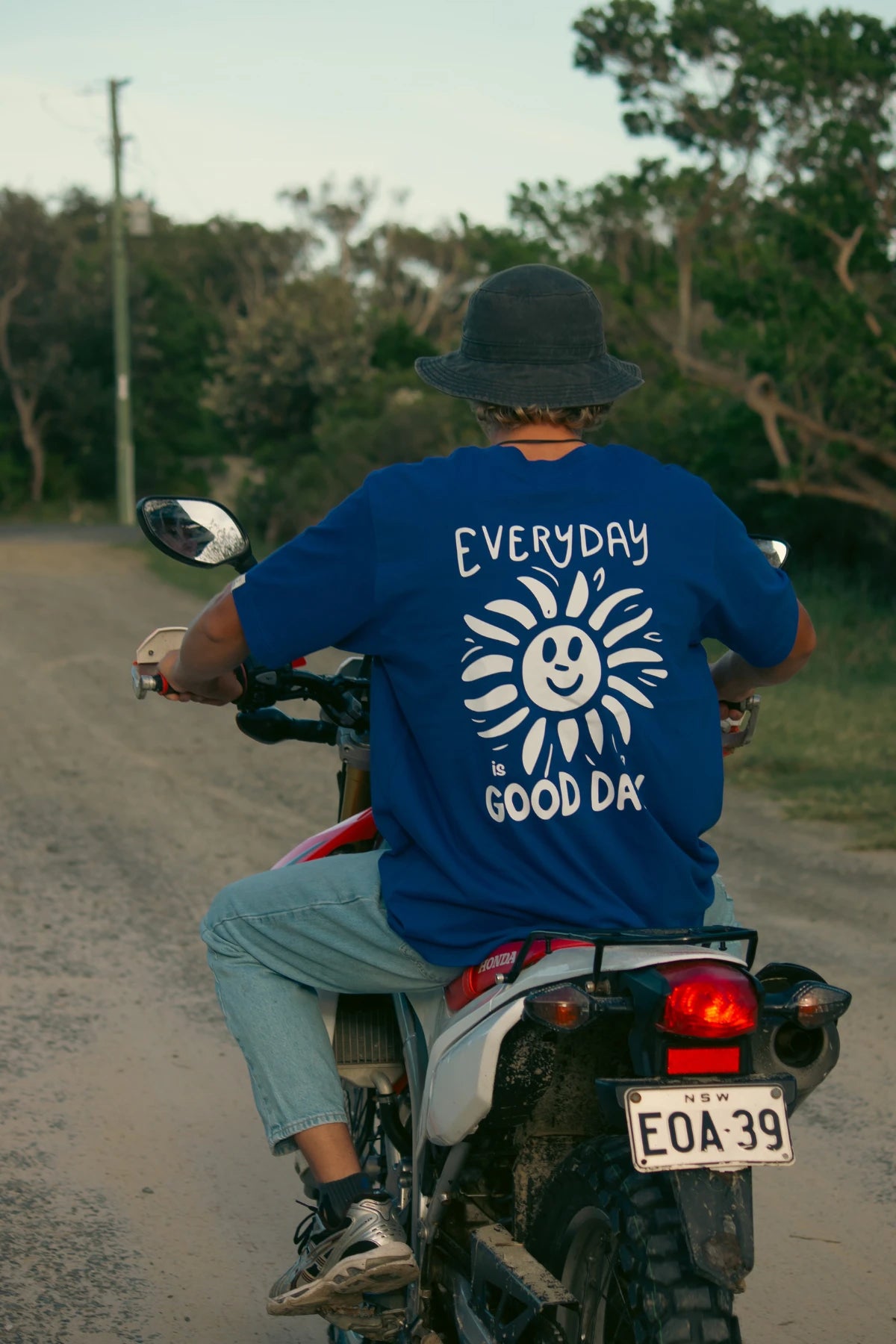 Rückansicht mit Sonnen-Print und Hut auf Offroad-Motorrad im Good Day Oversized T-Shirt in blau