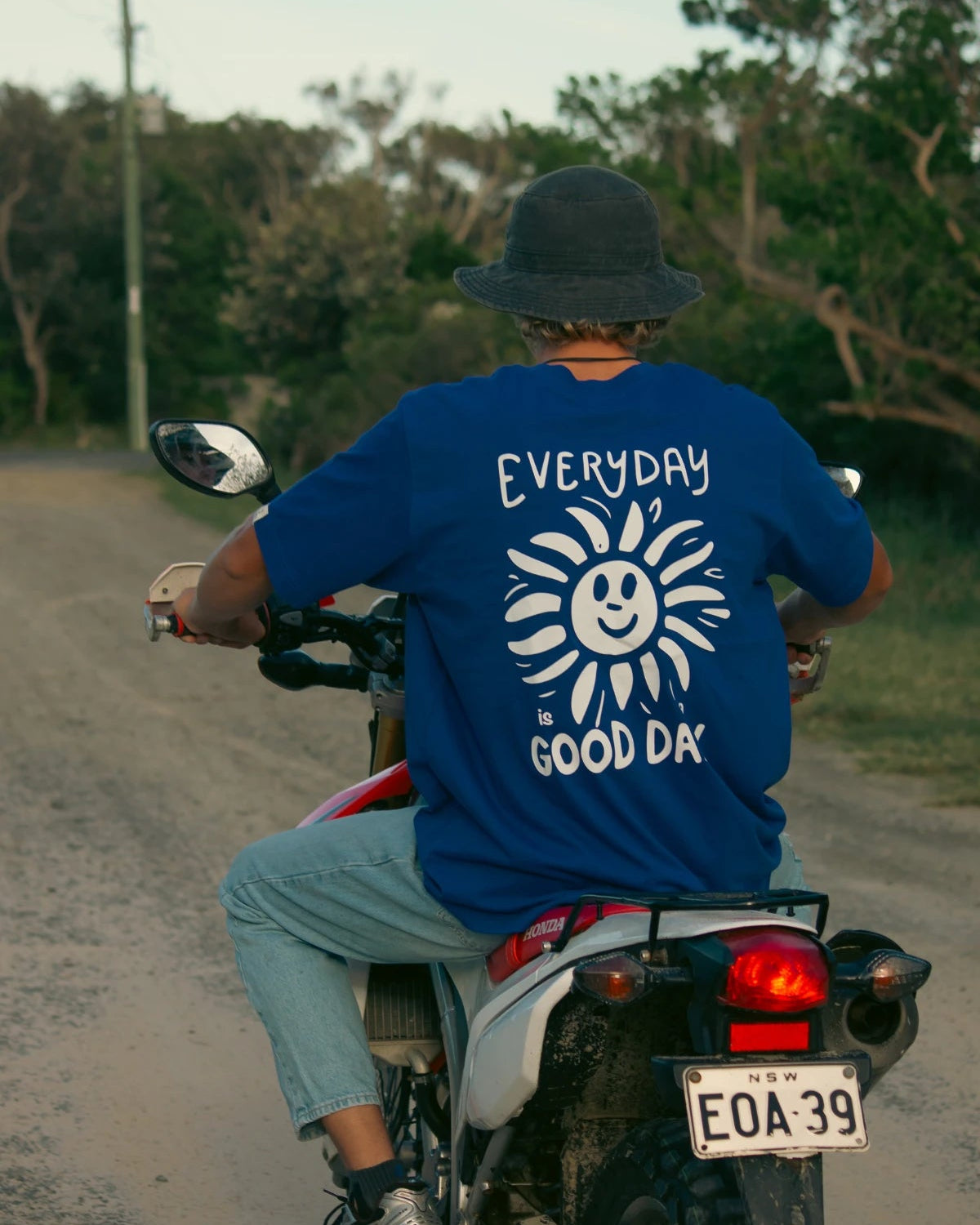 Rückansicht mit Sonnen-Print und Hut auf Offroad-Motorrad im Good Day Oversized T-Shirt in blau
