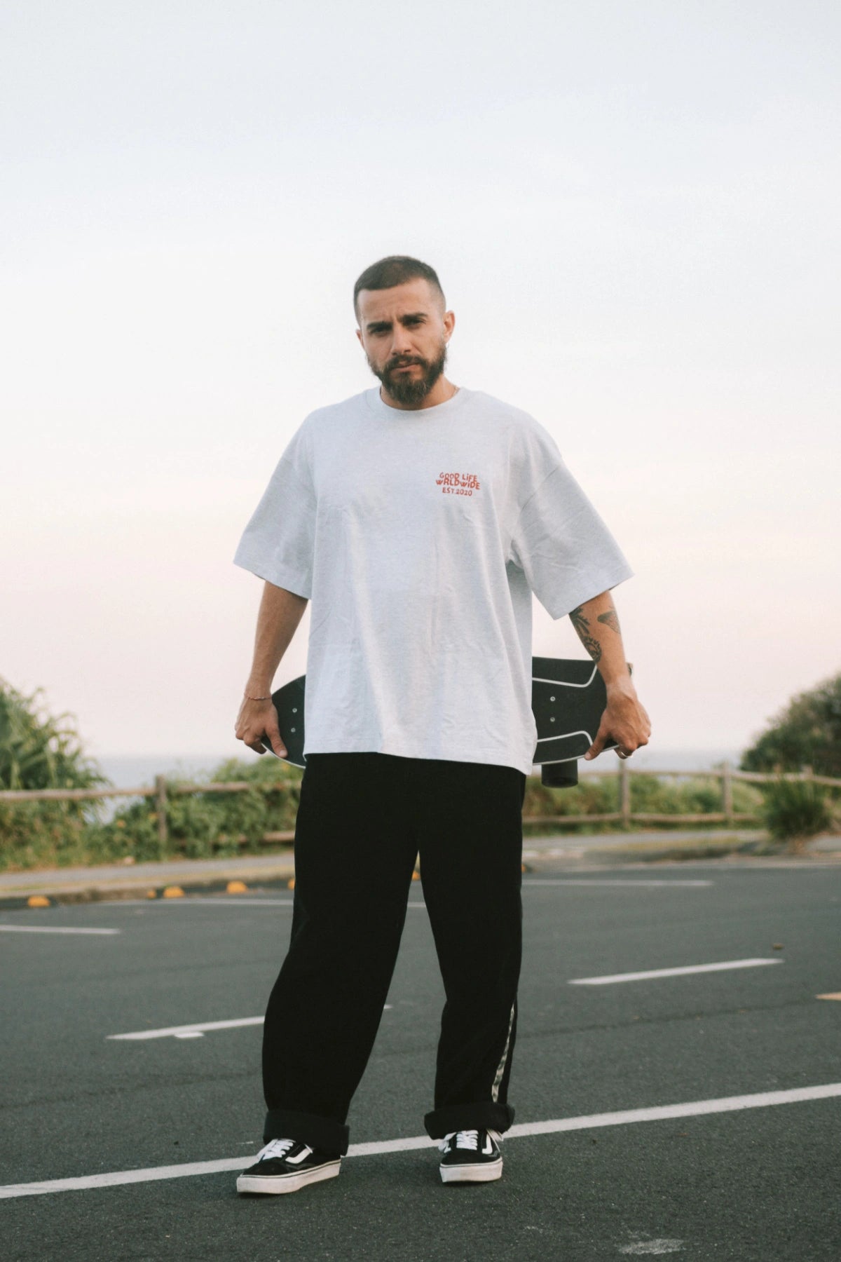 Mann trägt das Goodlife Heavy T-Shirt Cool Grey mit Frontprint „Good Life Worldwide“ – relaxter Surf-Vibe.