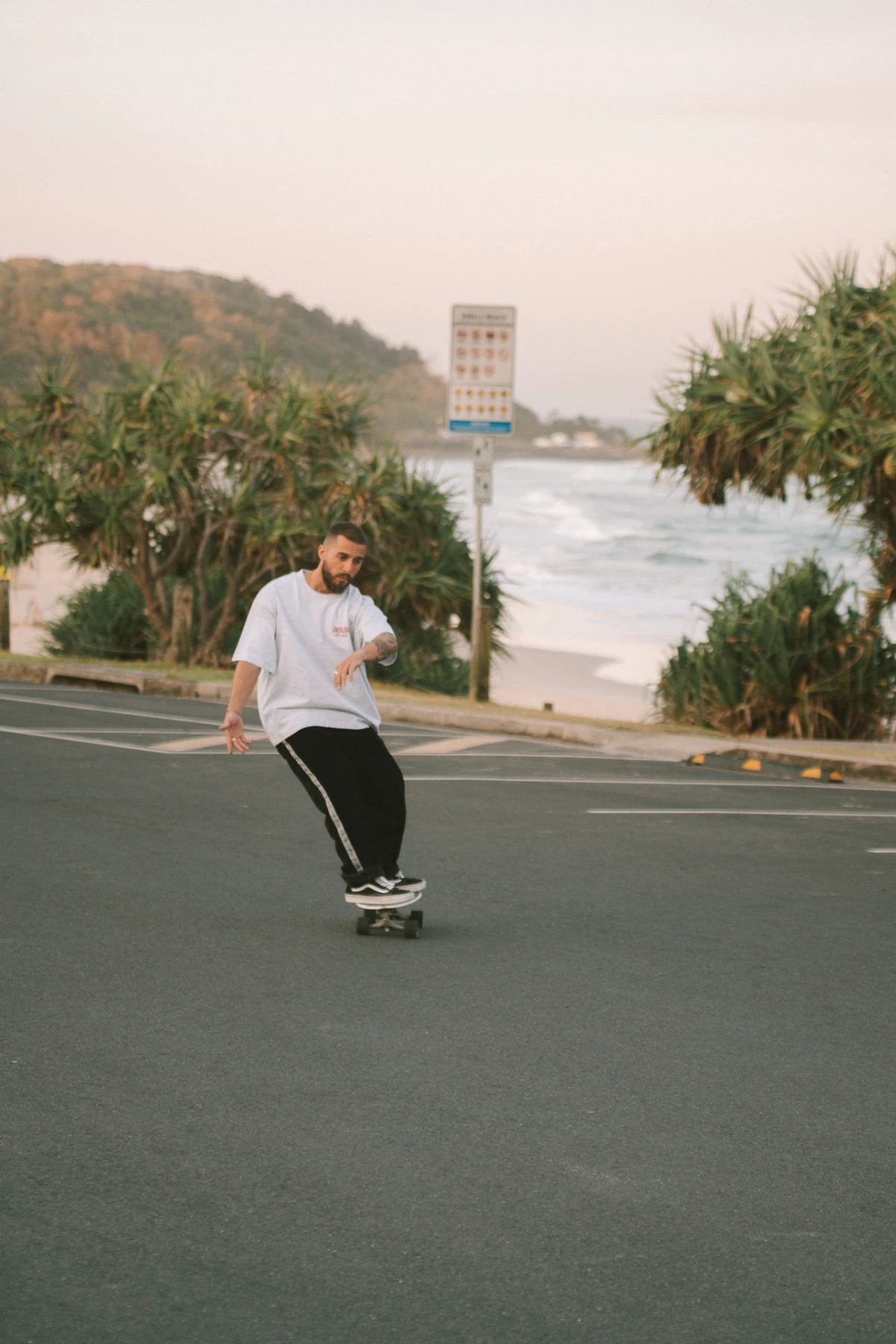 Lässiger Skater-Look – Mann im Goodlife Heavy T-Shirt Cool Grey von The Sunkissed Rebels mit Longboard.
