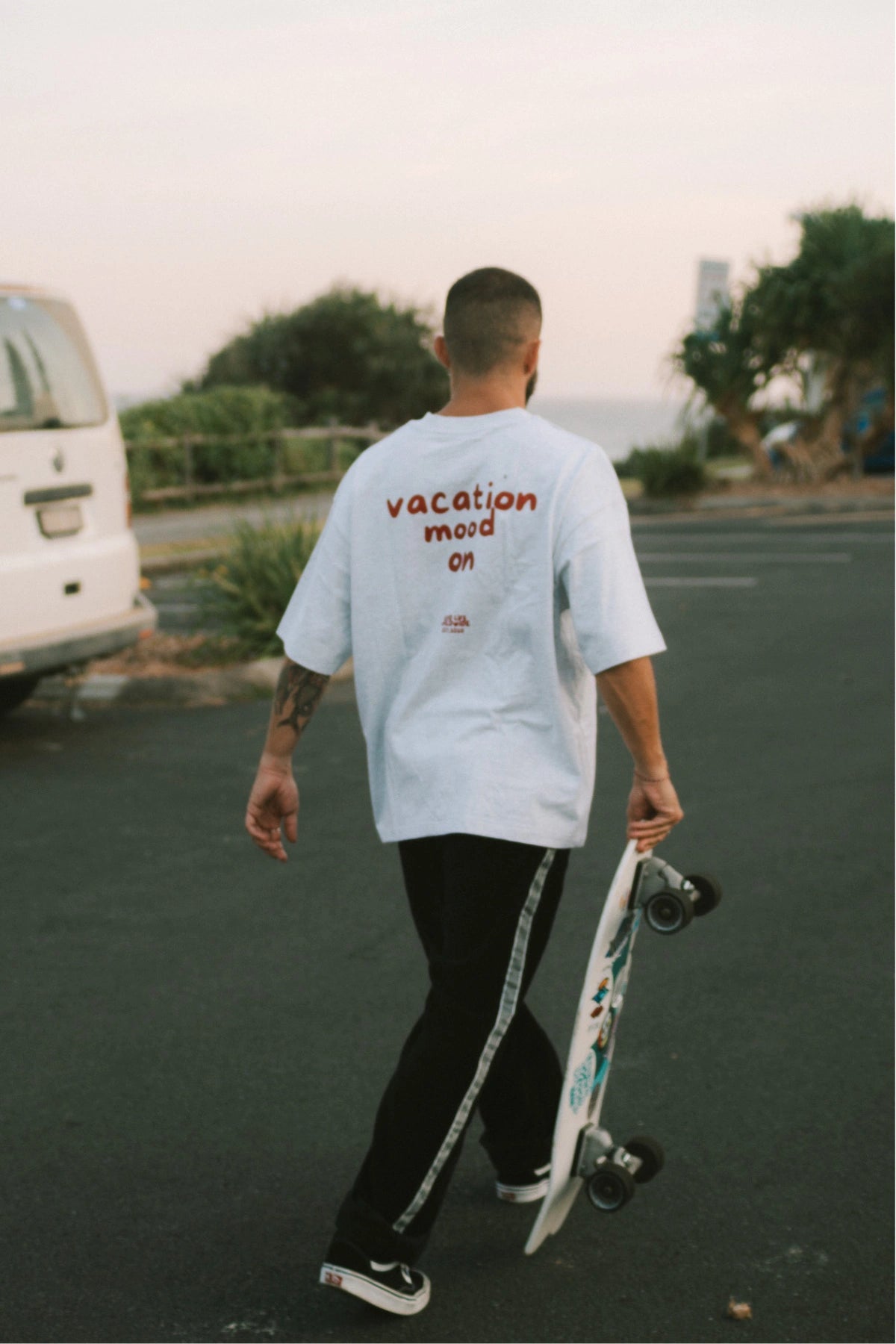 Rückansicht – Goodlife Heavy T-Shirt Cool Grey mit rotem Print „Vacation Mood On“ von The Sunkissed Rebels. Mann in bewegung