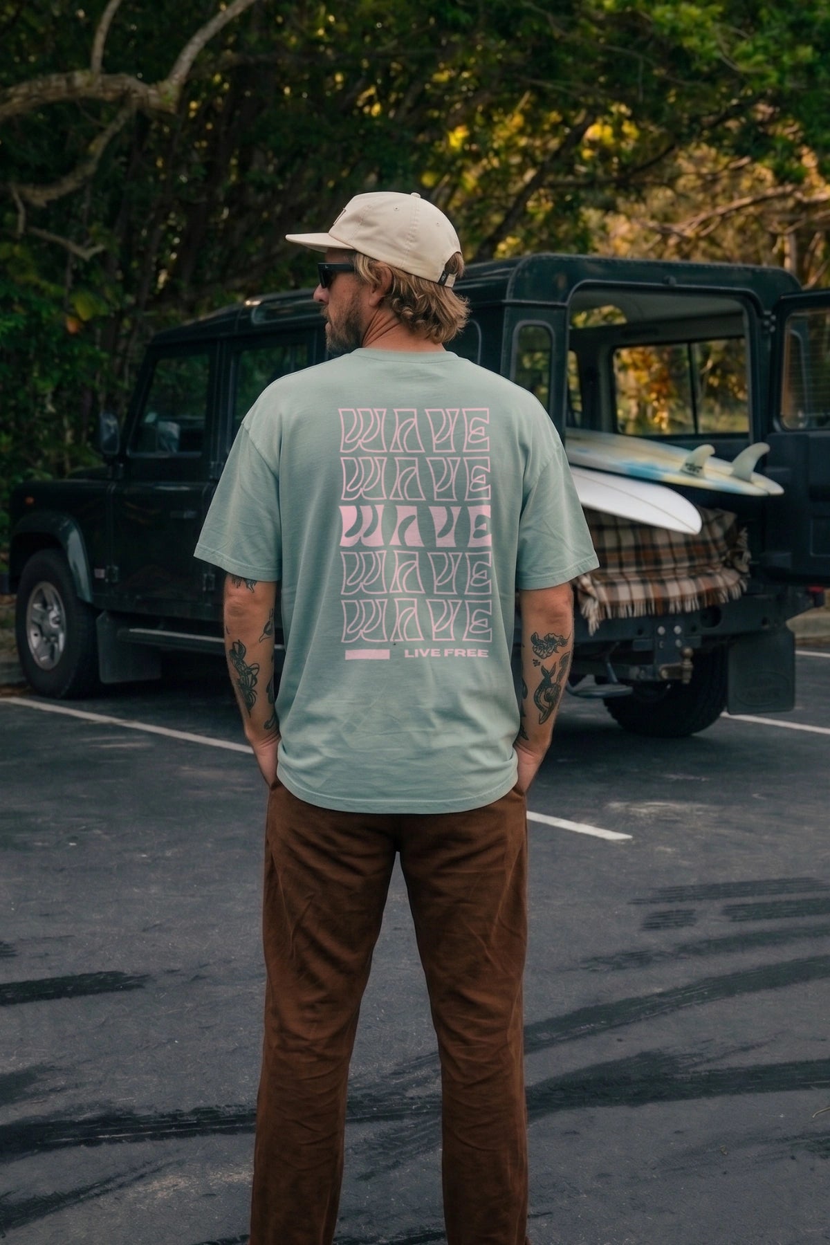 Mann trägt aloegrünes Live Free Oversized T-Shirt mit großem rosa Backprint von The Sunkissed Rebels
