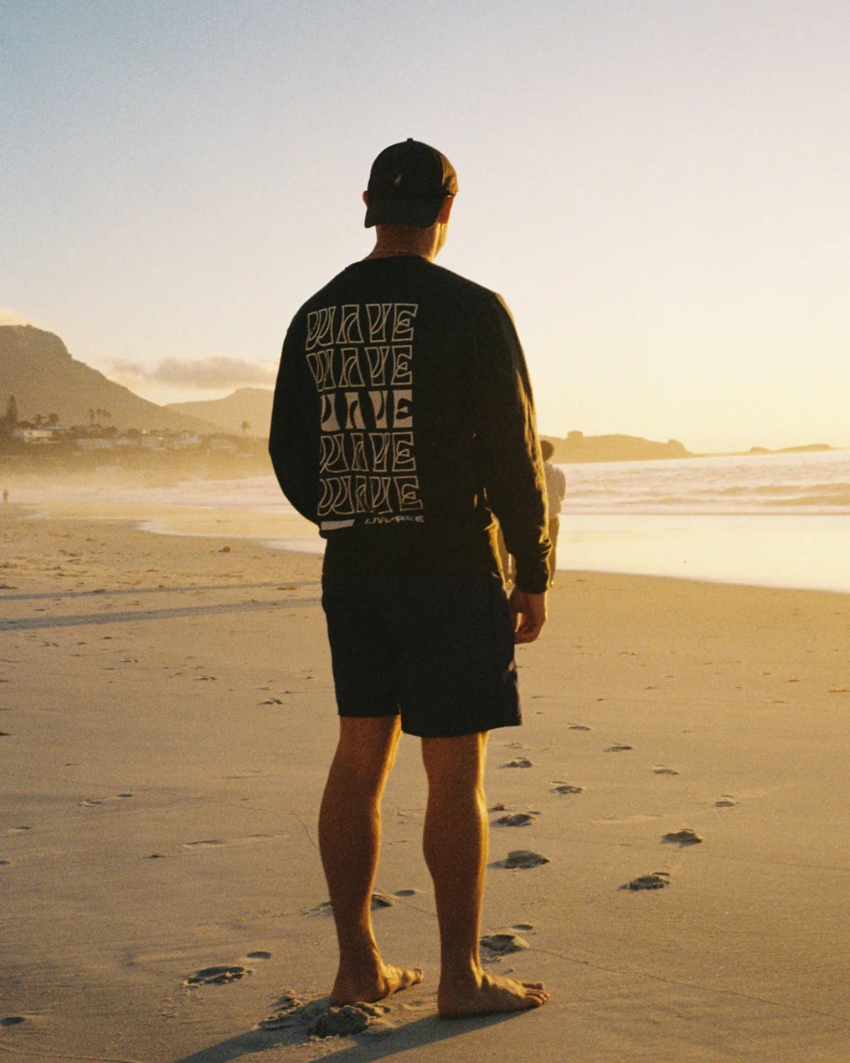 Model trägt Live Free Vintage Sweater Black am Strand bei Sonnenuntergang – nachhaltige Streetwear von The Sunkissed Rebels