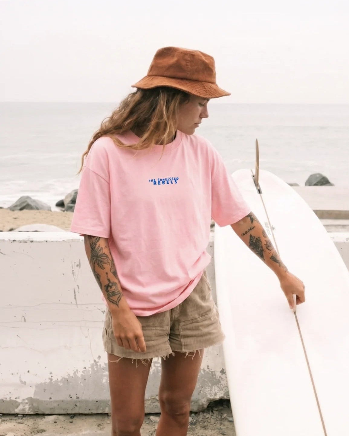 Frau am Strand im rosa No Bullshit Whale Boxy Oversized T-Shirt von The Sunkissed Rebels mit blauem Logo-Print auf der Brust