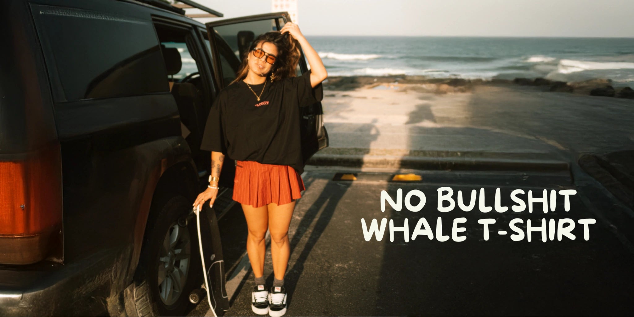 Person mit Skateboard neben Van am Strand im Sonnenlicht, trägt schwarzes No Bullshit Whale T-Shirt – Surf & Skate Lifestyle Shooting