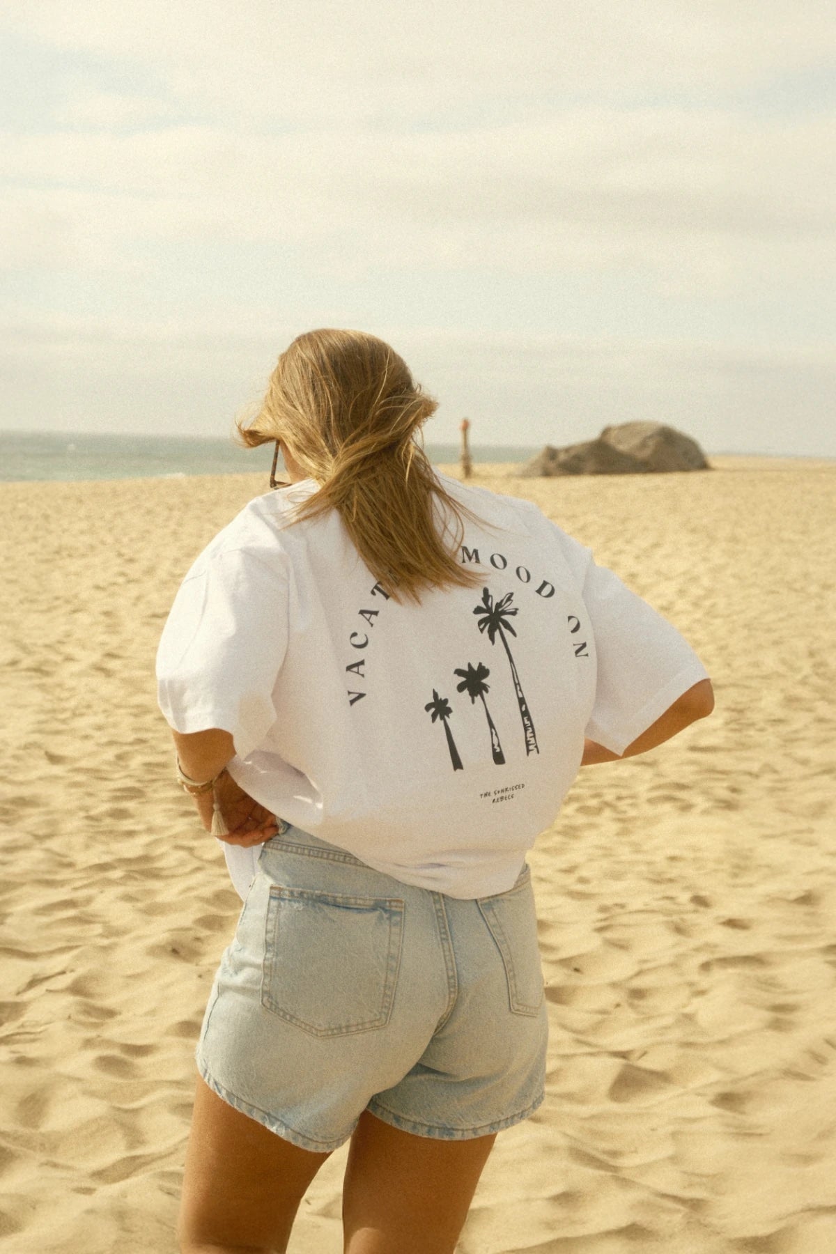 Windy beach look with Vacation Mood On palm shirt in front of a calm sea and natural boulder backdrop