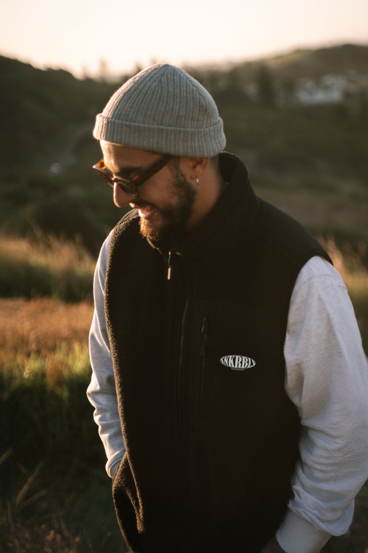 Mann steht auf Hügel bei Sonnenuntergang und trägt schwarze outdoor Weste