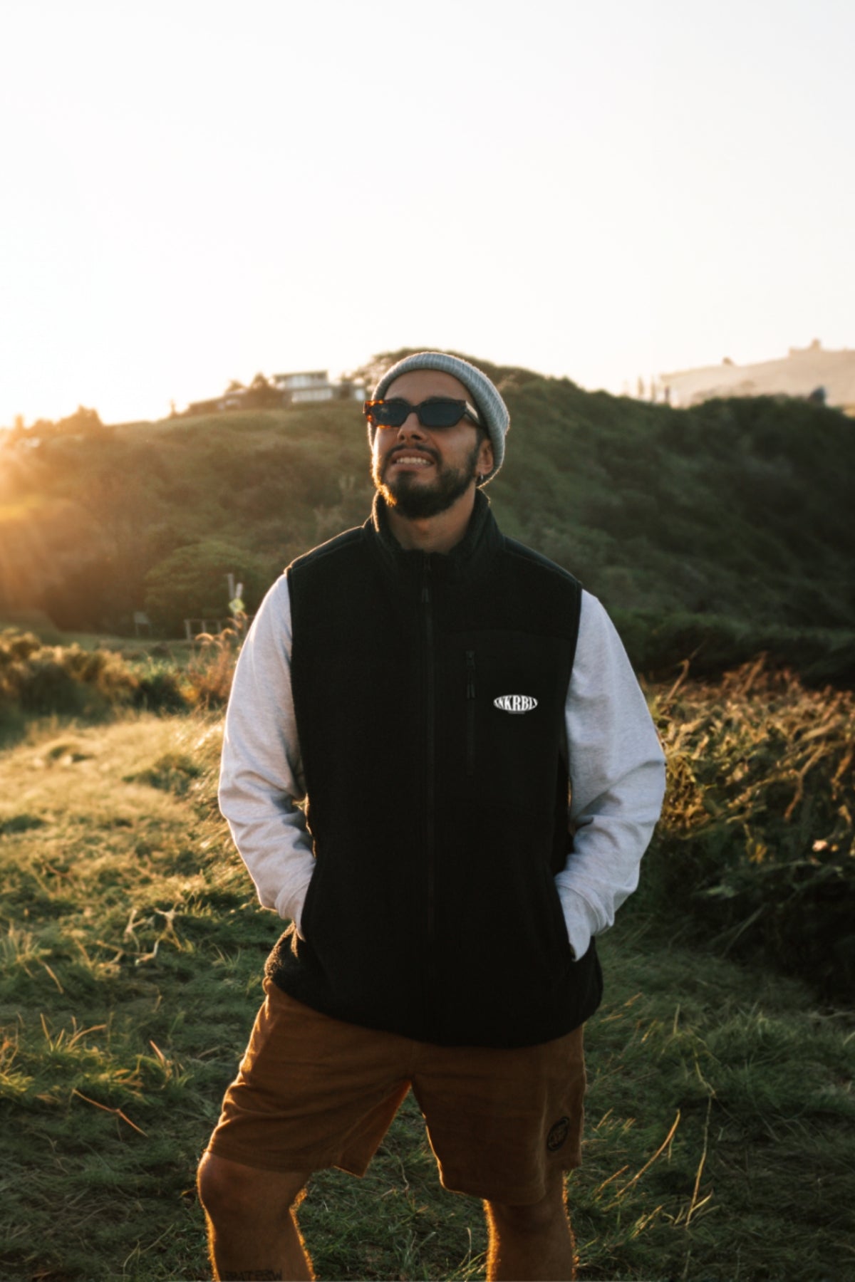 Mann steht auf Hügel bei Sonnenuntergang und trägt schwarze outdoor Weste