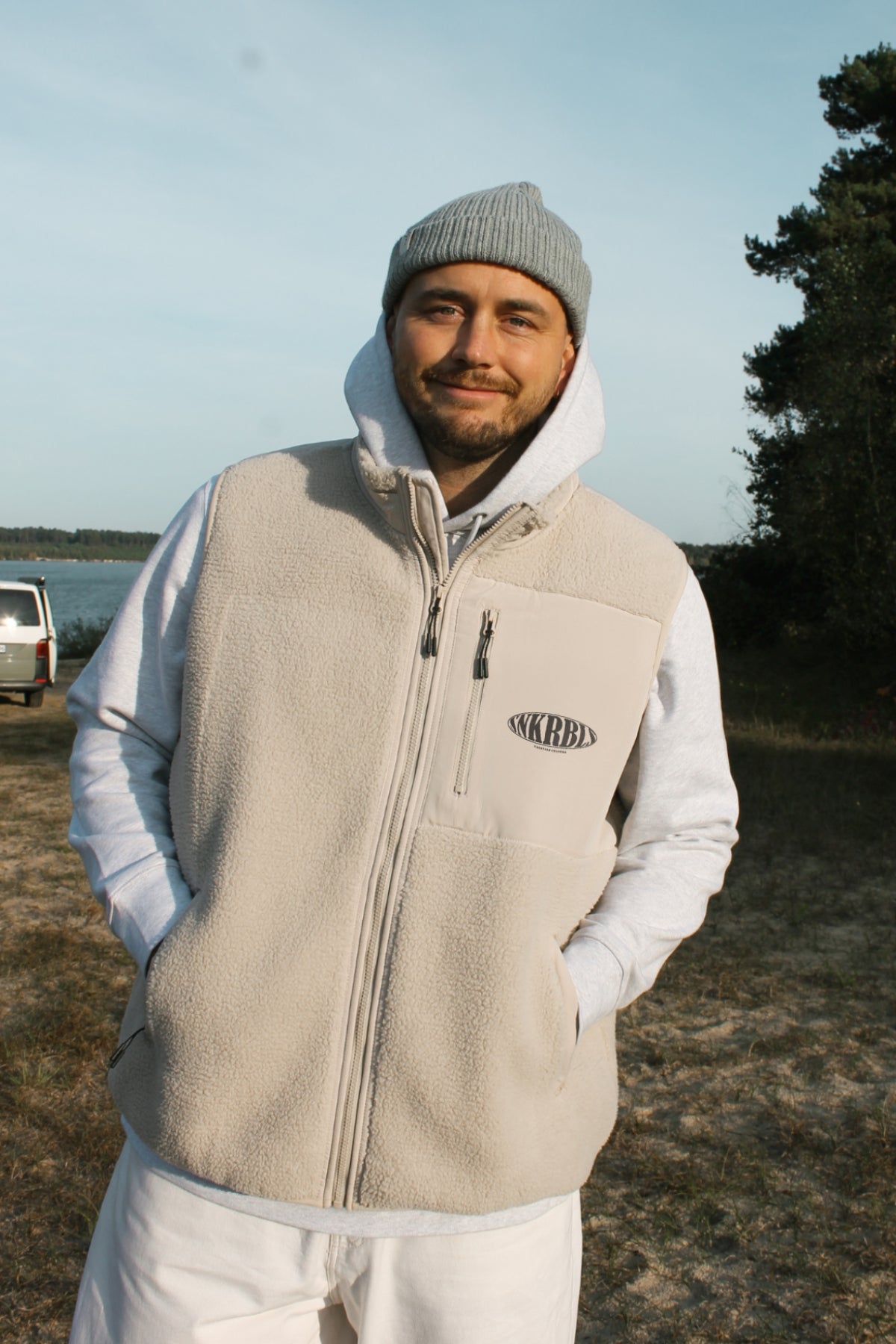 Reisender steht vor Bulli und trägt Beanie und Fleece Weste