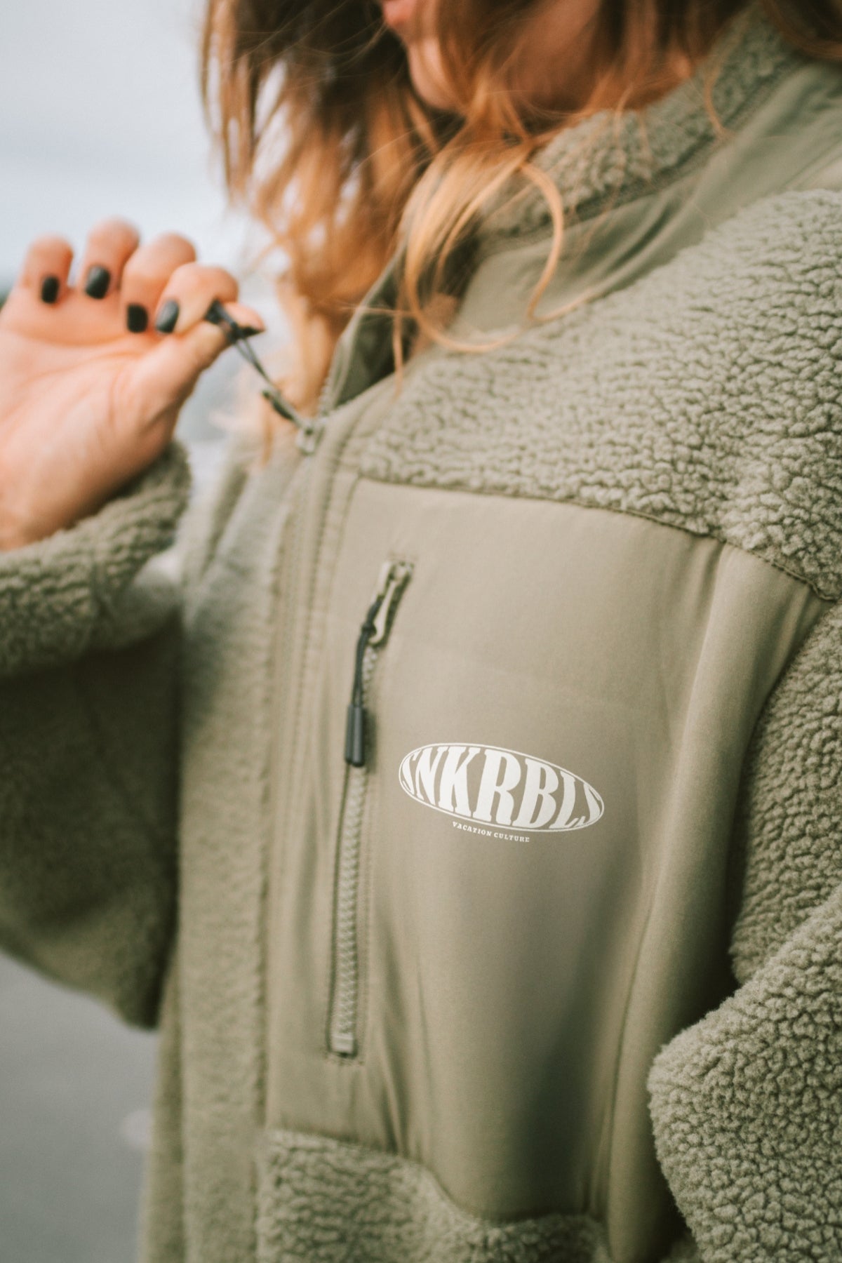 frau macht reisverschluss zu, trägt grüne fleecejacke Nahaufnahme