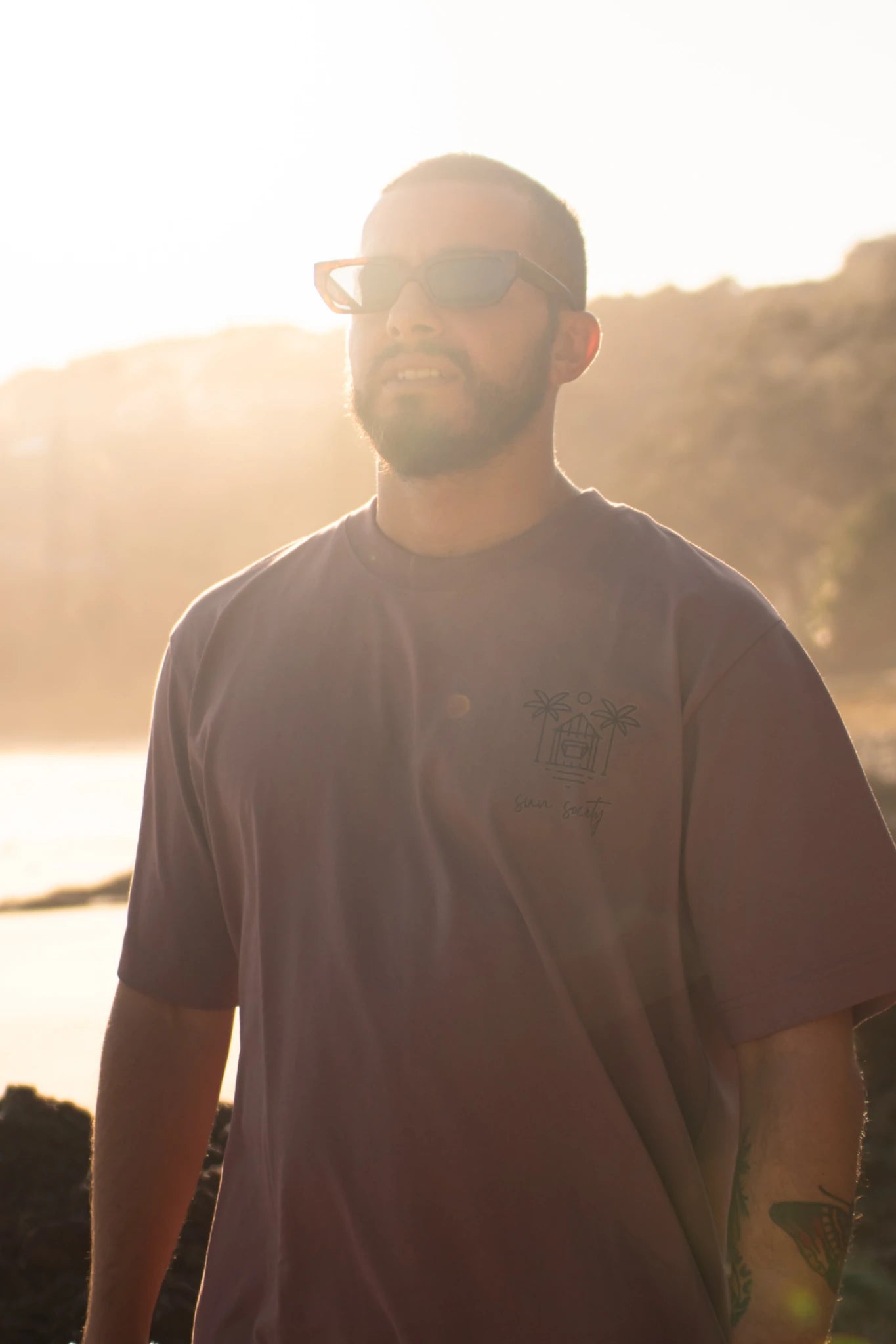 Frontansicht des Oversized T-Shirt Açaí Sun Society von The Sunkissed Rebels bei goldenem Sonnenlicht am Meer