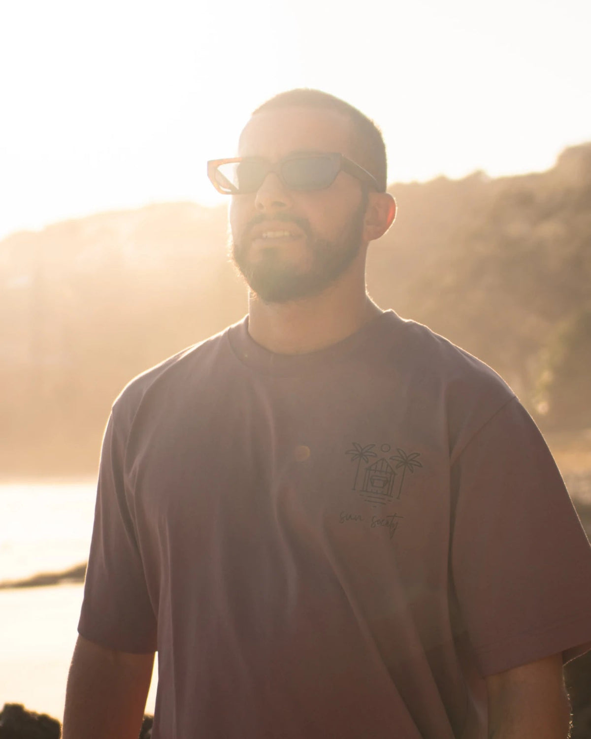 Frontansicht des Oversized T-Shirt Açaí Sun Society von The Sunkissed Rebels bei goldenem Sonnenlicht am Meer
