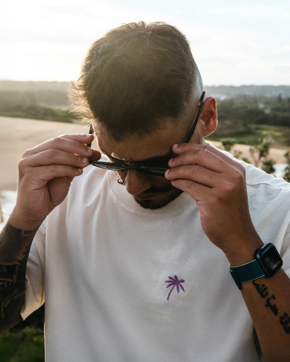 ahaufnahme Oversized T-Shirt mit Palmen-Stick, Mann setzt Sonnenbrille auf