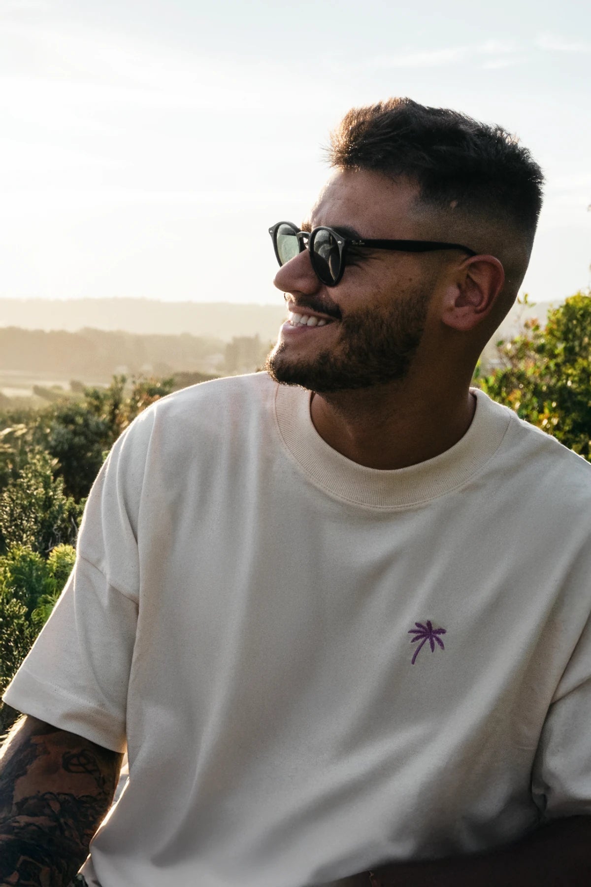 Lachender Mann im Oversized T-Shirt Natural Raw mit Sonnenbrille im Sonnenlicht
