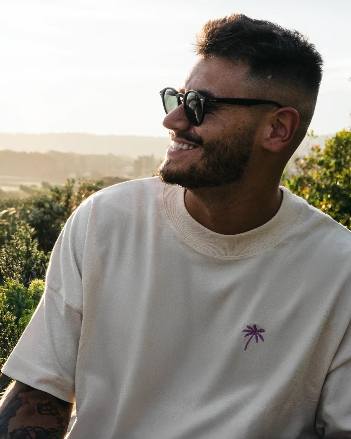 Lachender Mann im Oversized T-Shirt Natural Raw mit Sonnenbrille im Sonnenlicht