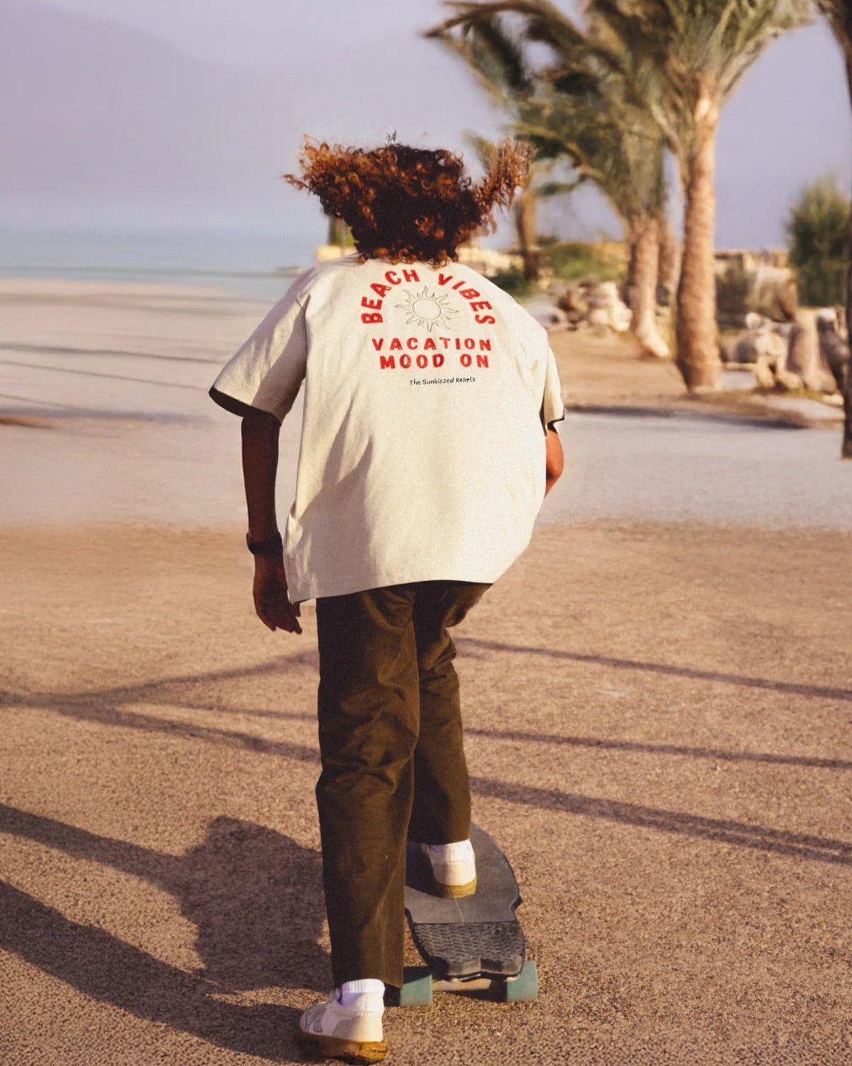 Mann trägt Sand Beach Vibes Shirt bei Sonnenuntergang auf Skaterplatz – The Sunkissed Rebels