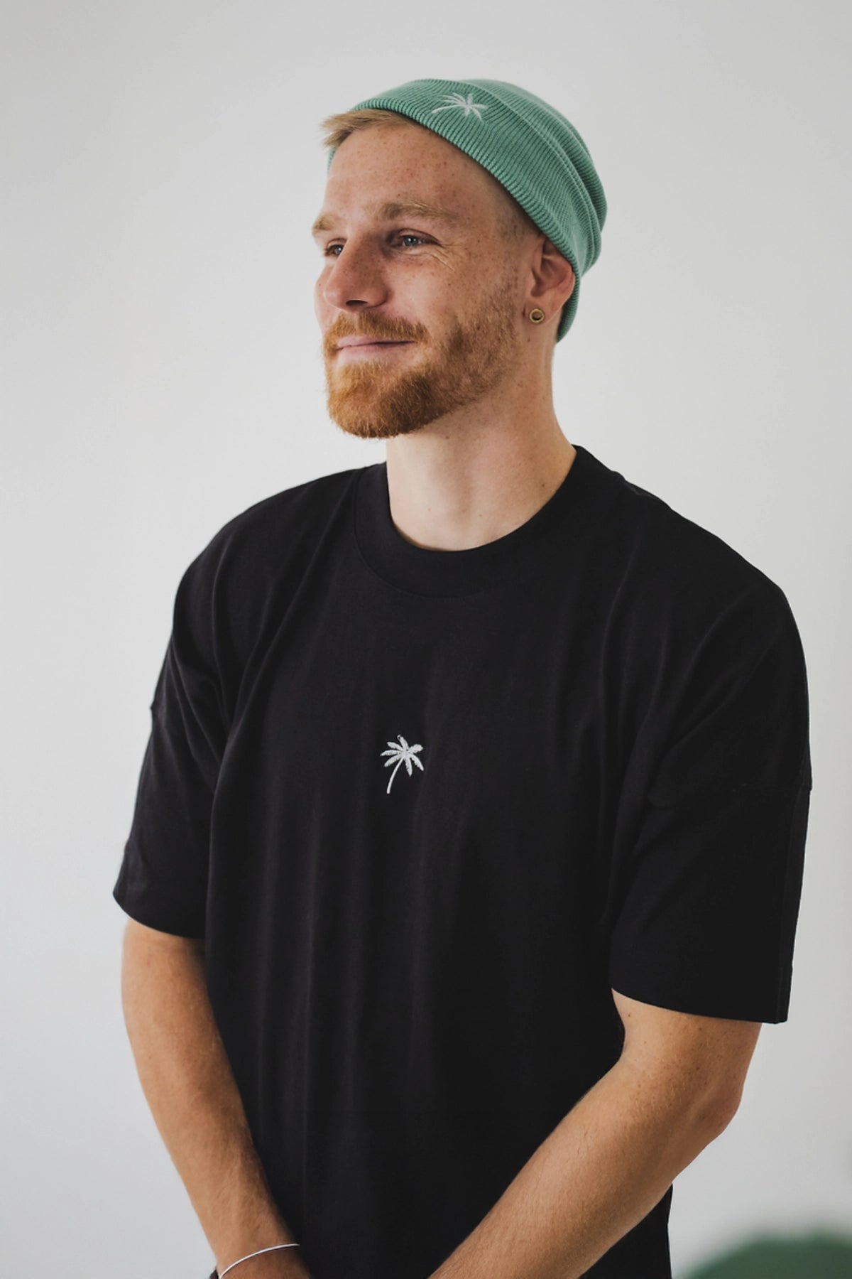 Mann im schwarzen Oversized T-Shirt mit gestickter weißer Palme von The Sunkissed Rebels – Studioaufnahme