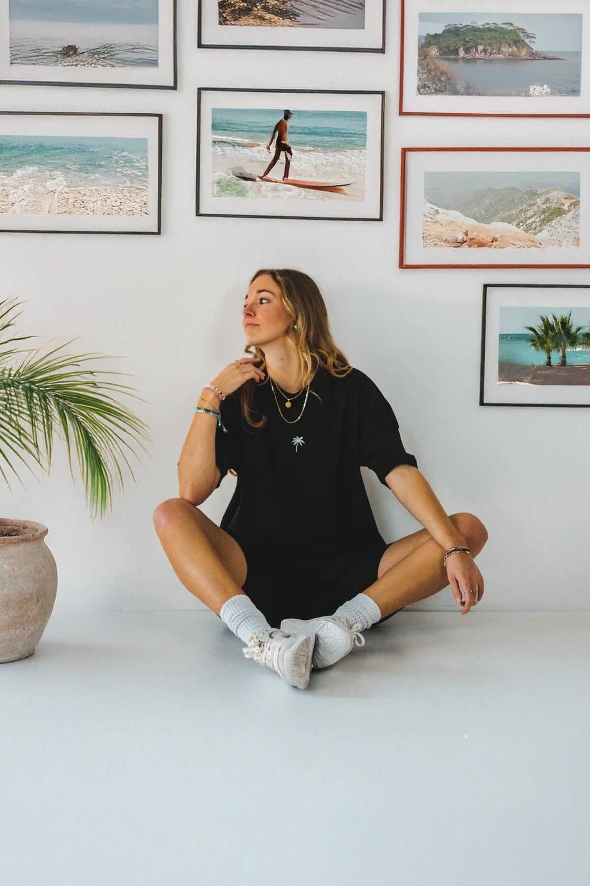 Frau trägt schwarzes Oversized T-Shirt mit Palmenlogo von The Sunkissed Rebels – Indoor-Lifestyle