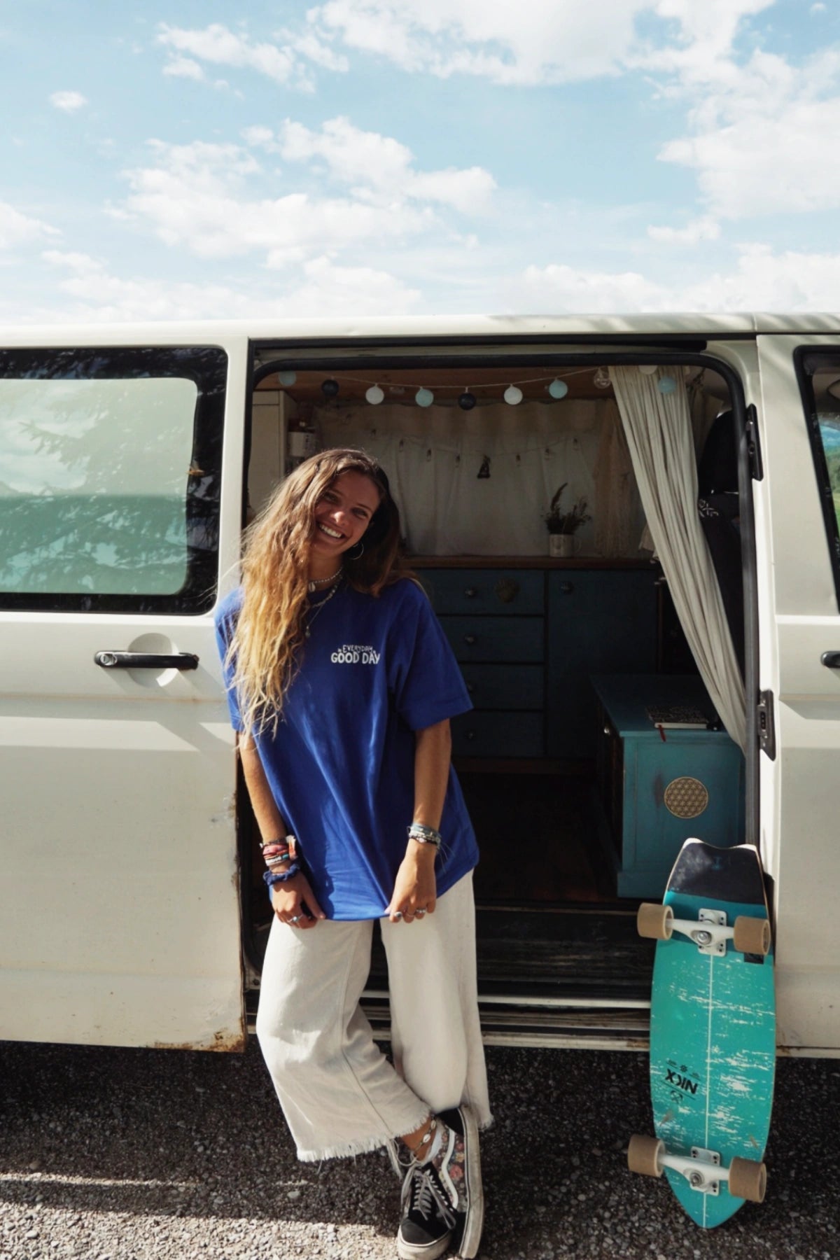 Junge Frau mit Skateboard neben Camper, im Fokus ein nachhaltiges Oversized T-Shirt mit Feelgood-Statement