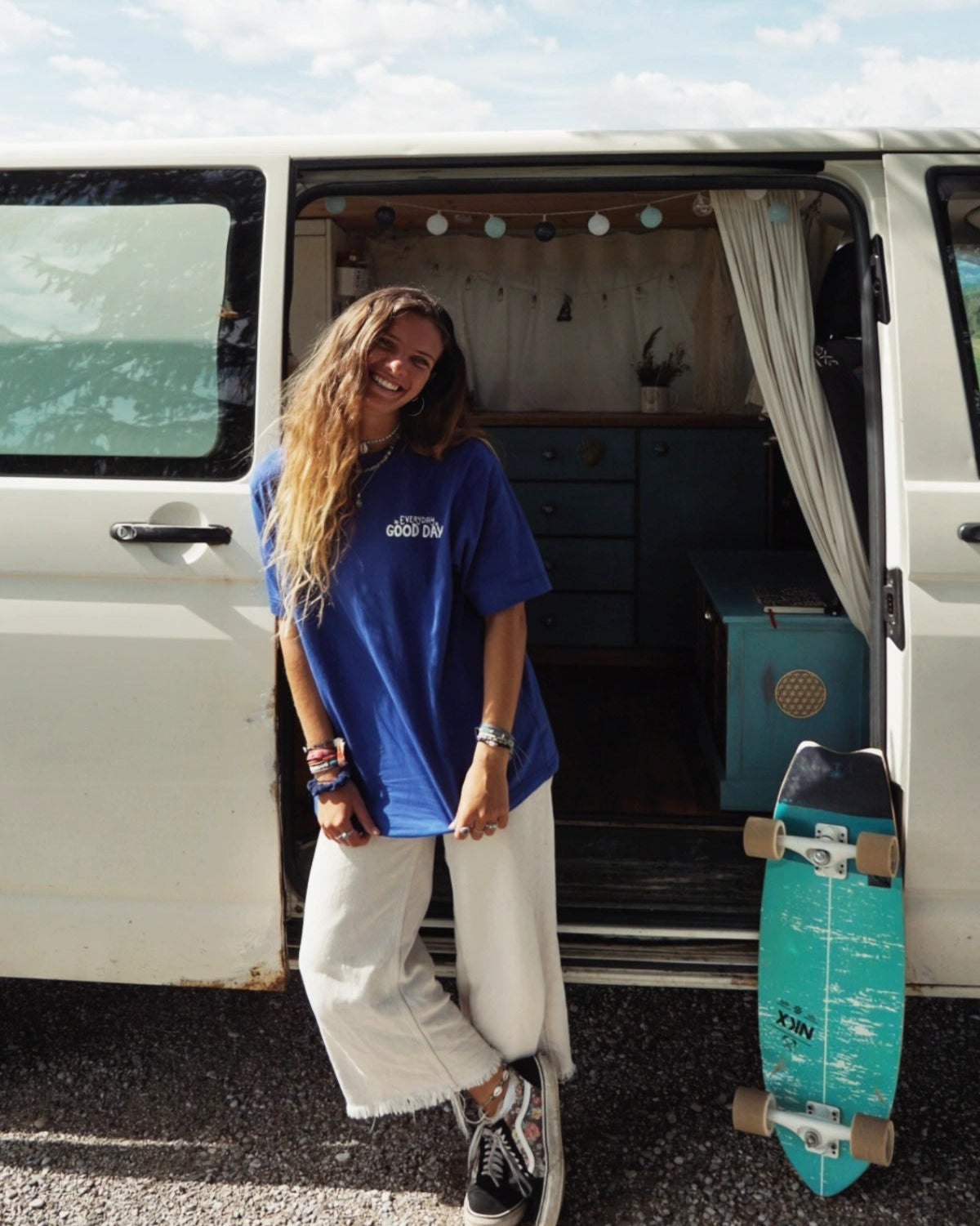 Junge Frau mit Skateboard neben Camper, im Fokus ein nachhaltiges Oversized T-Shirt mit Feelgood-Statement