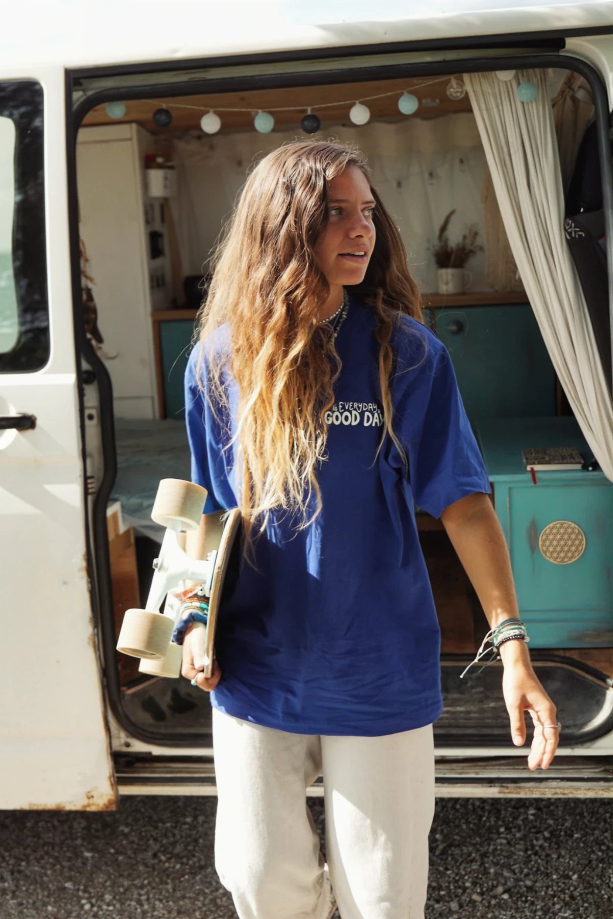 Junge Frau mit Skateboard neben Camper, im Fokus ein nachhaltiges Oversized T-Shirt mit Feelgood-Statement