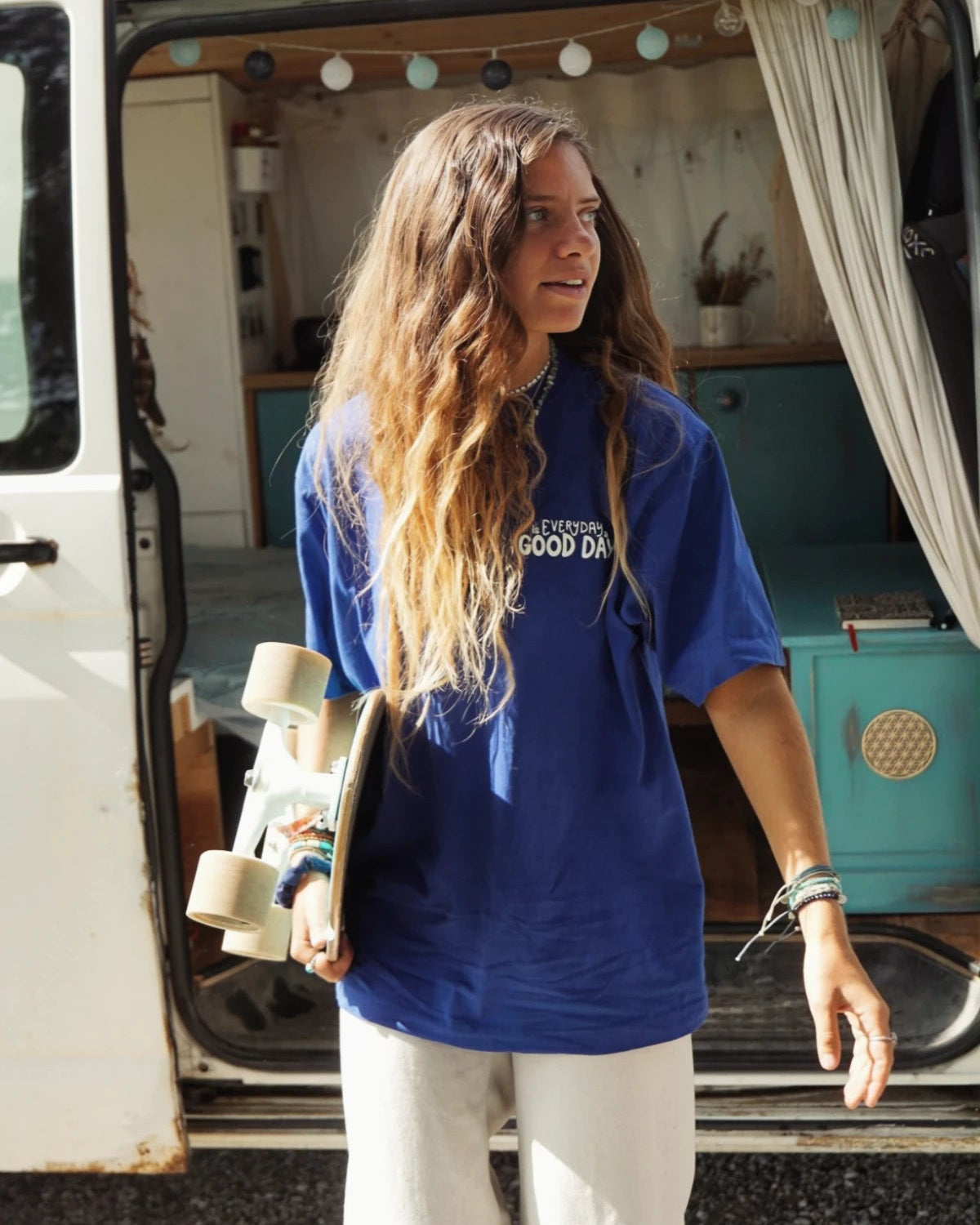 Junge Frau mit Skateboard neben Camper, im Fokus ein nachhaltiges Oversized T-Shirt mit Feelgood-Statement