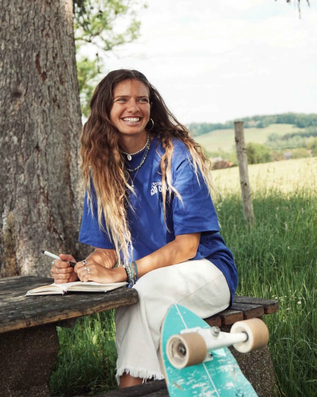 Frau sitzt an einem Picknicktisch im Grünen, trägt lockeres Statement-Shirt mit „Everyday is a Good Day“