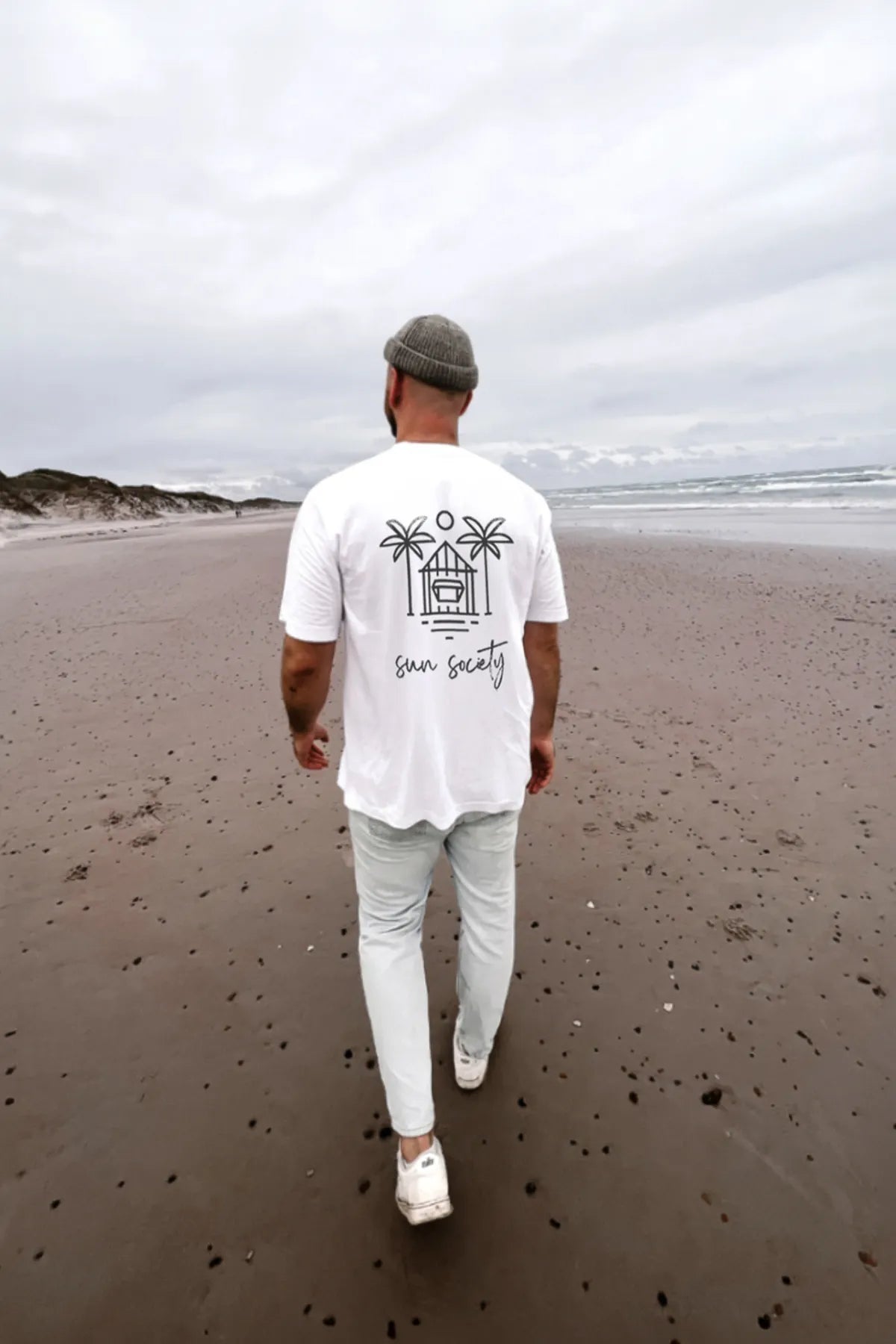 Mann am Strand trägt Oversized T-Shirt in weiß mit Sun Society Print Rückansicht
