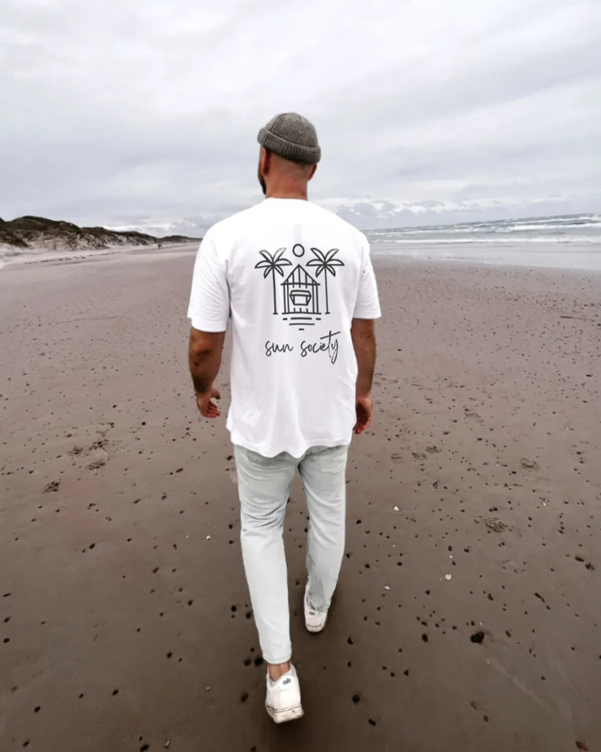 Mann am Strand trägt Oversized T-Shirt in weiß mit Sun Society Print Rückansicht