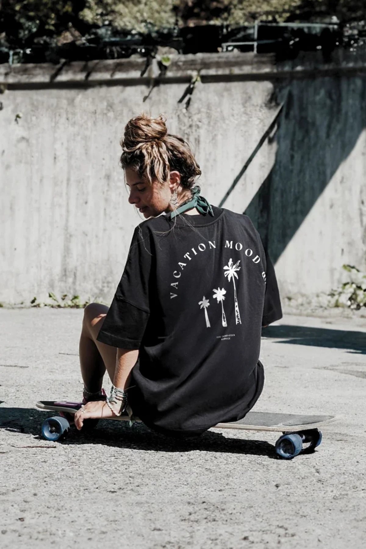 Backprint des Vacation Mood On T-Shirts in Schwarz – Frau sitzt auf Skateboard