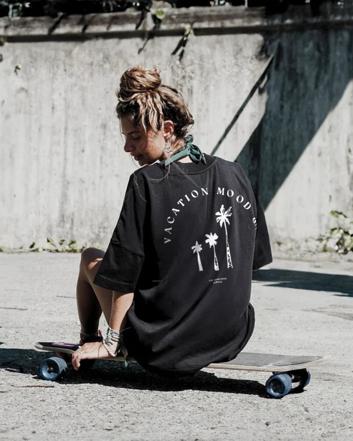 Backprint des Vacation Mood On T-Shirts in Schwarz – Frau sitzt auf Skateboard