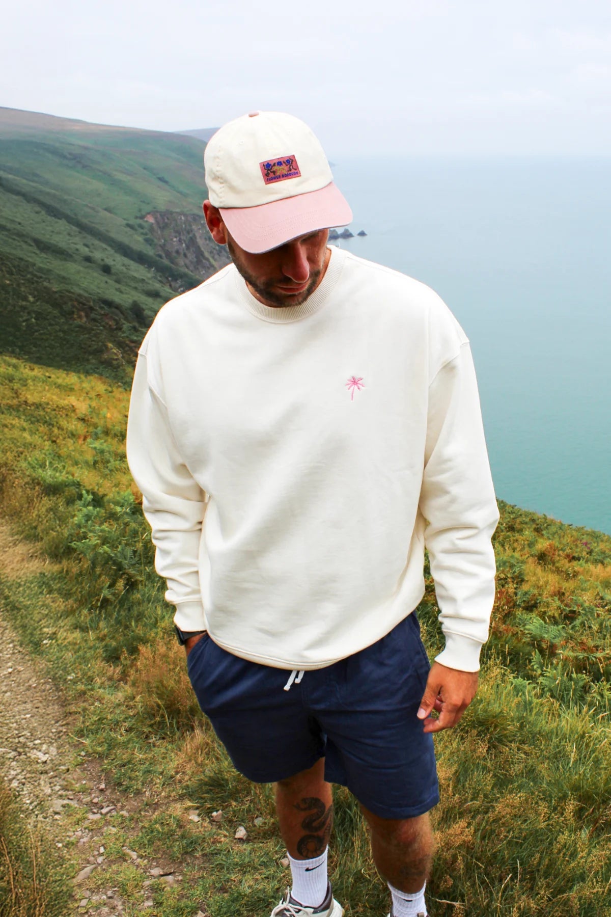 Nahaufnahme des cremefarbenen Sweaters mit rosa Palmenstickerei auf der Brust.