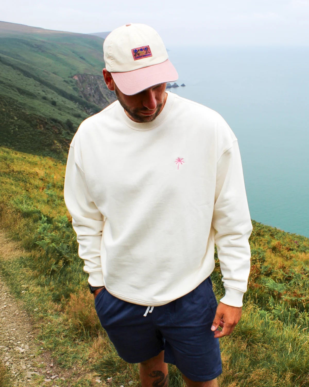 Nahaufnahme des cremefarbenen Sweaters mit rosa Palmenstickerei auf der Brust.