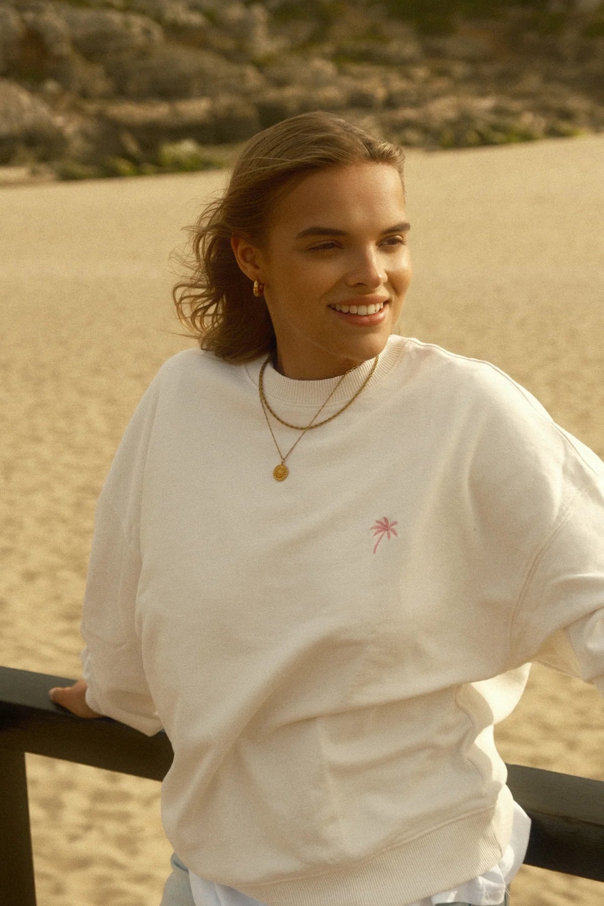 Frau mit Palm Tree Oversized Sweater – Cream am Strand, lachend und entspannt.
