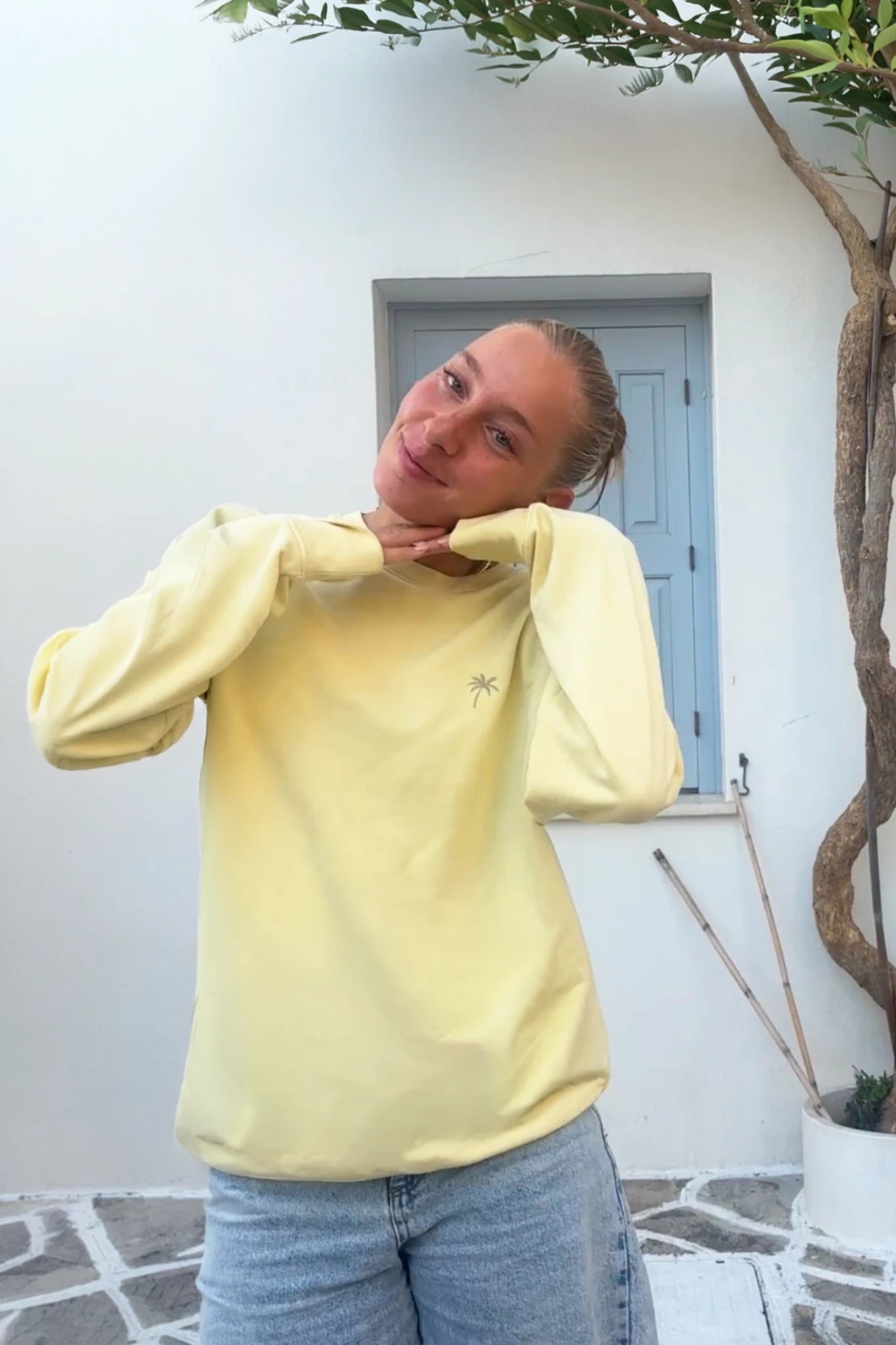 Nahaufnahme einer Frau im gelben Palm Tree Sweater Butter – minimalistisches Design mit kleinem Palmenlogo