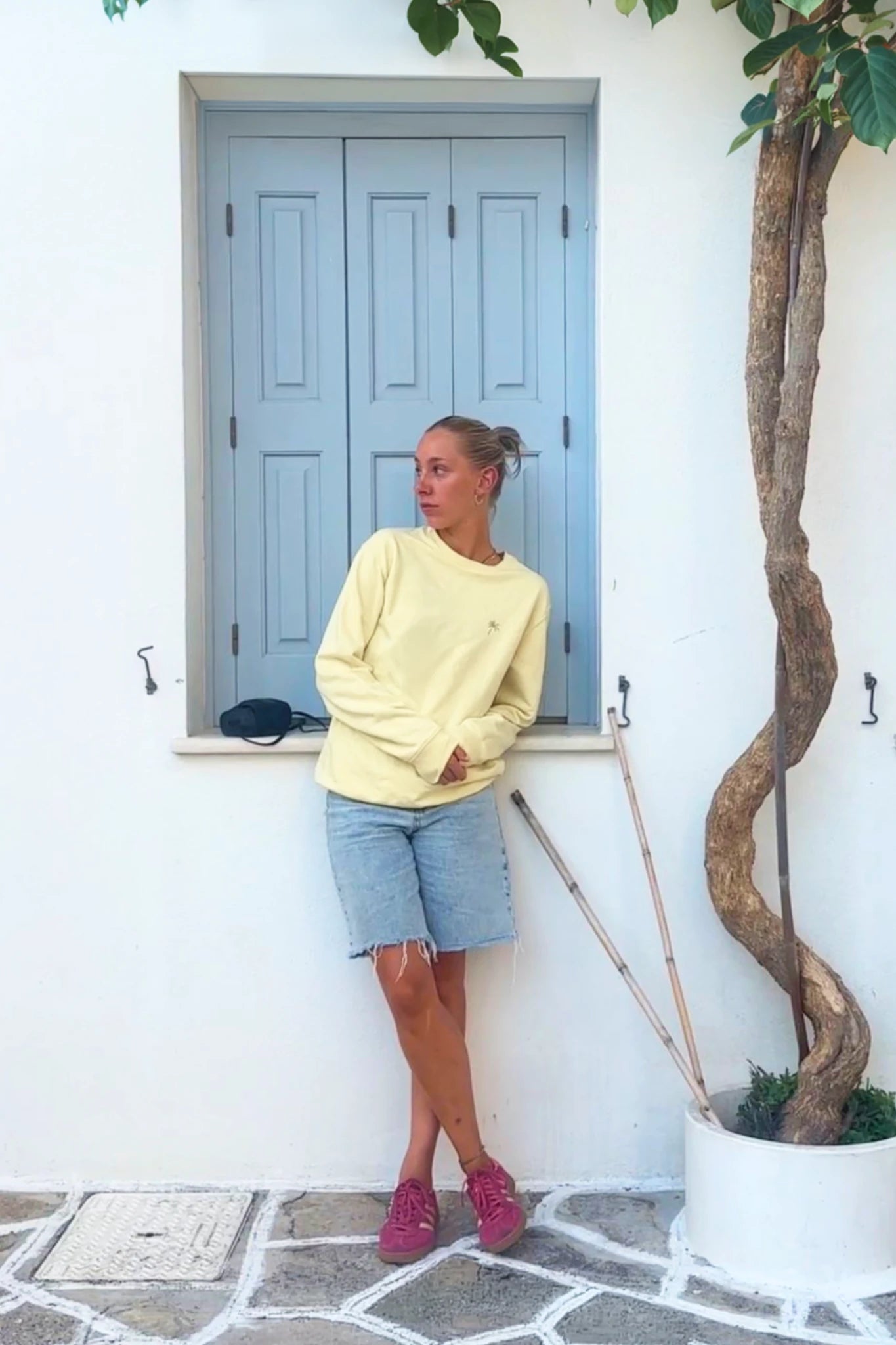 Frau steht vor weißer Wand und trägt gelben Palm Tree Sweater in Butter – lässiger Oversized Look mit Sommer Vibes