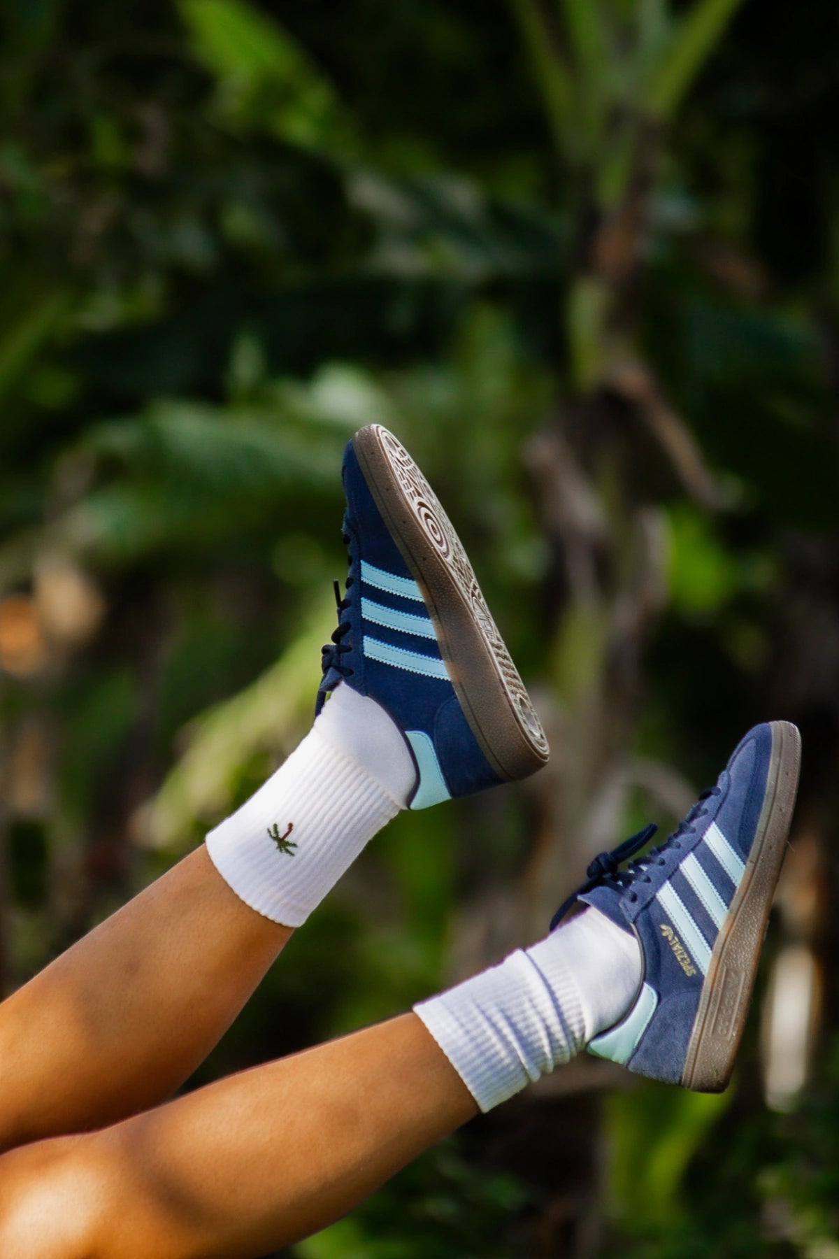 Weiße Tennissocken mit gestickter Palme im Casual-Look mit blauen Sneakern im Sitzen getragen