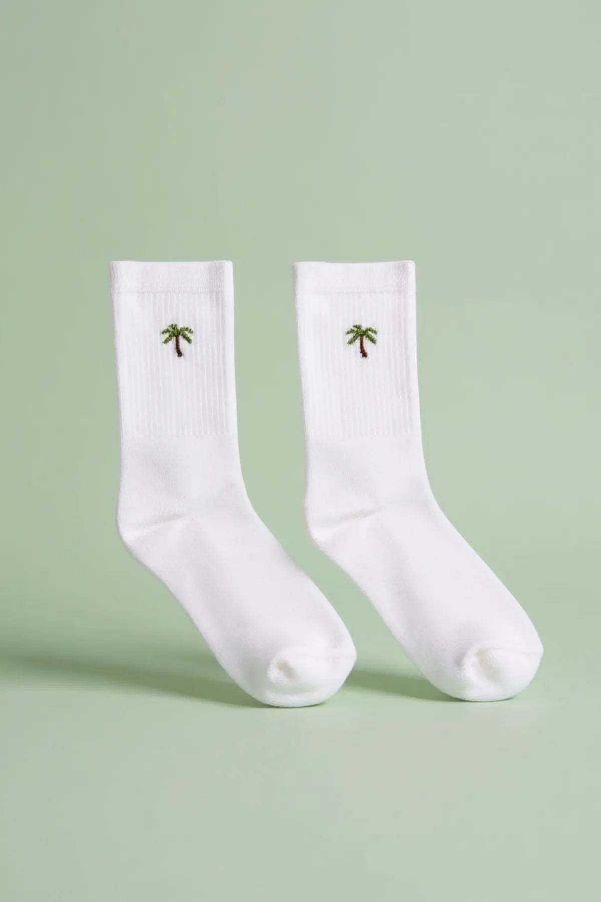 Weiße Tennissocken als Paar mit gestickter grüner Palme auf dem Schaft.