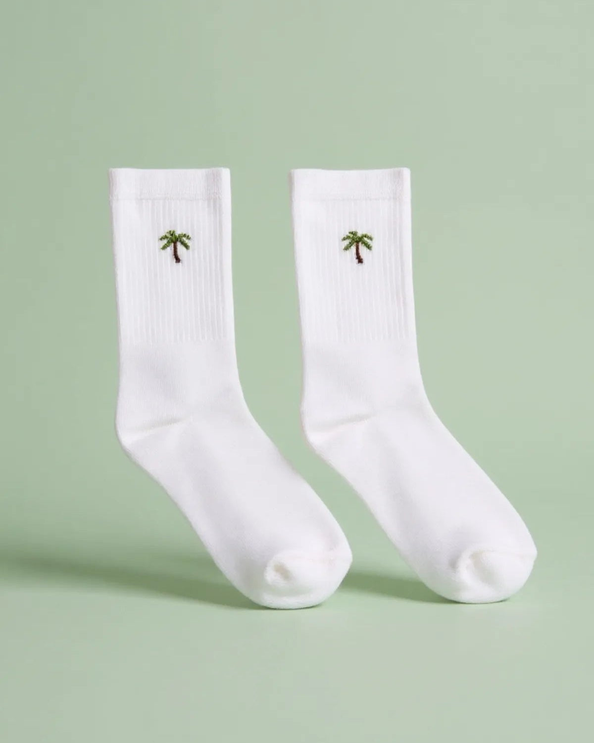 Weiße Tennissocken als Paar mit gestickter grüner Palme auf dem Schaft.