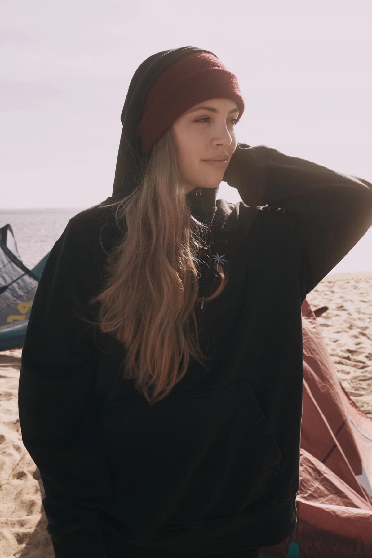 Model von The Sunkissed Rebels trägt den Palm Tree Vintage Hoodie Black bei Sonnenlicht am Strand
