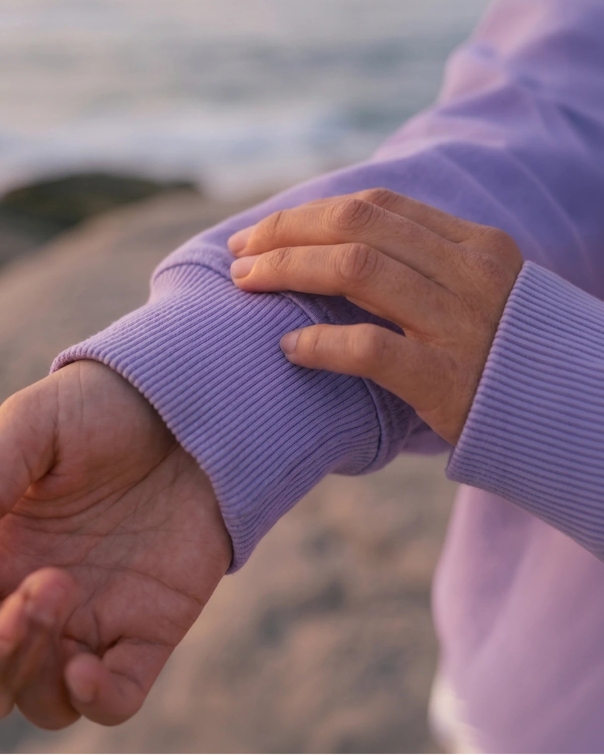 Detailaufnahme des Pink Palm Oversized Vintage Sweater Violet mit weichem Stoff und oversized Ärmel am Strand bei Sonnenuntergang
