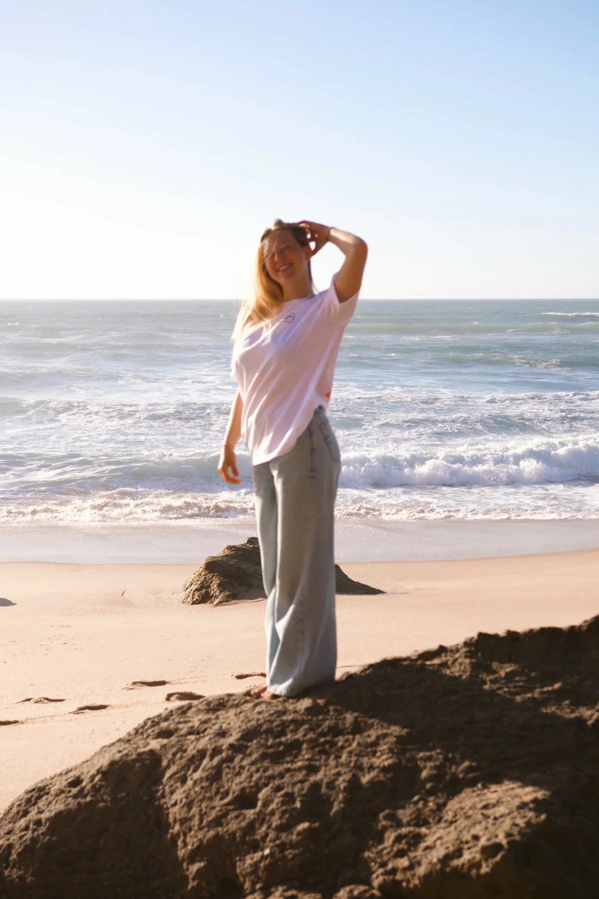 Frontalansicht des weißen The Rebel Elements Light T-Shirts kombiniert mit einer hellen Wide-Leg-Jeans am Strand für den perfekten Vacation-Look.
