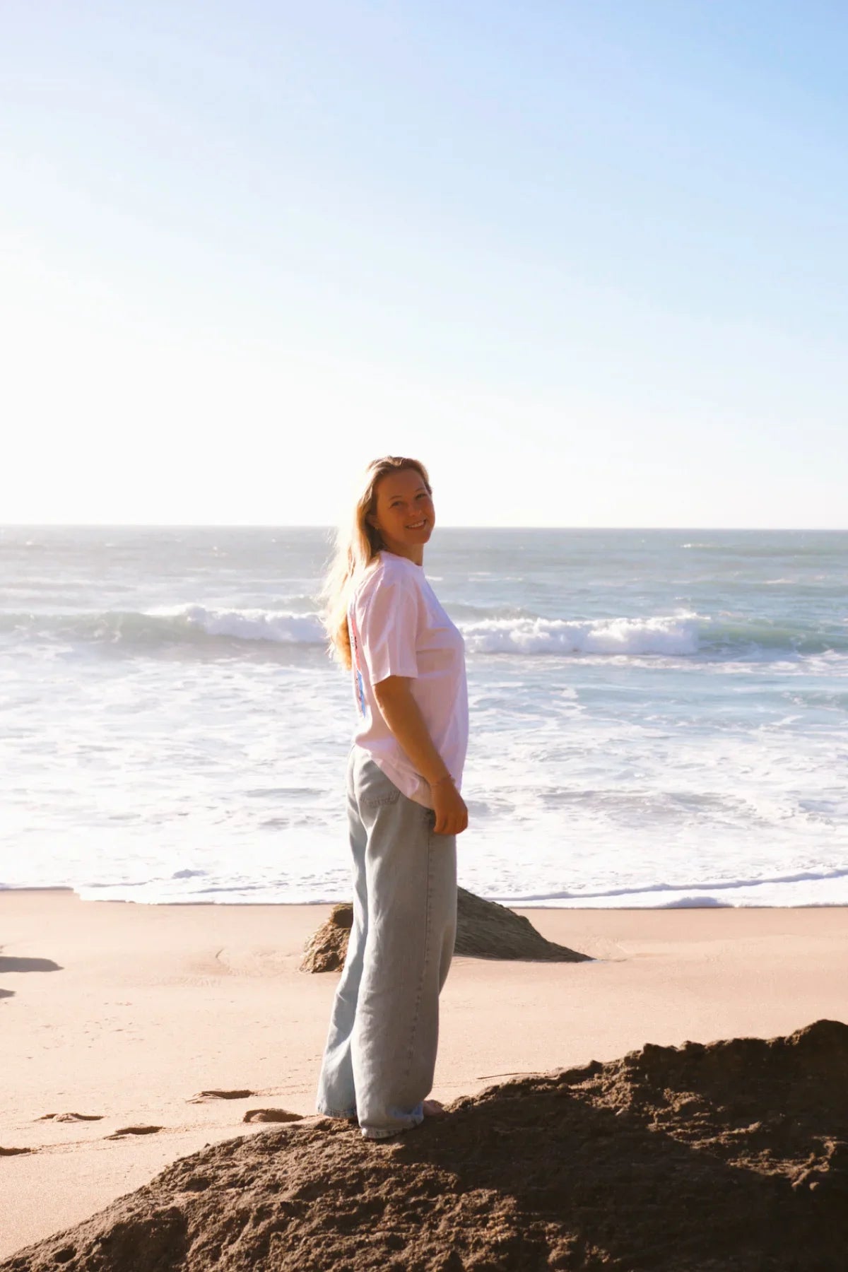 Seitenansicht des weißen The Rebel Elements Light T-Shirts kombiniert mit einer hellen Wide-Leg-Jeans am Strand für den perfekten Vacation-Look.